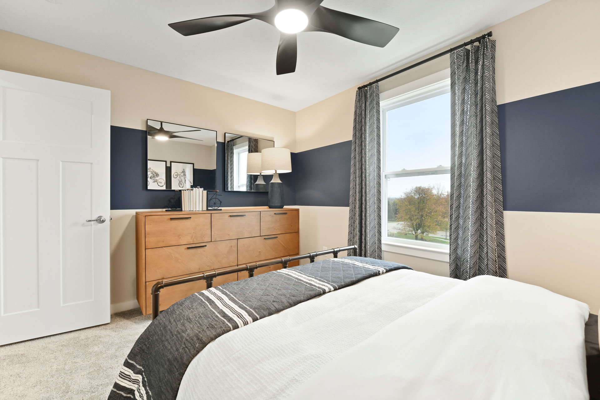 Modern bedroom interior featuring a wooden dresser, striped bedding, and a large window with natural light.