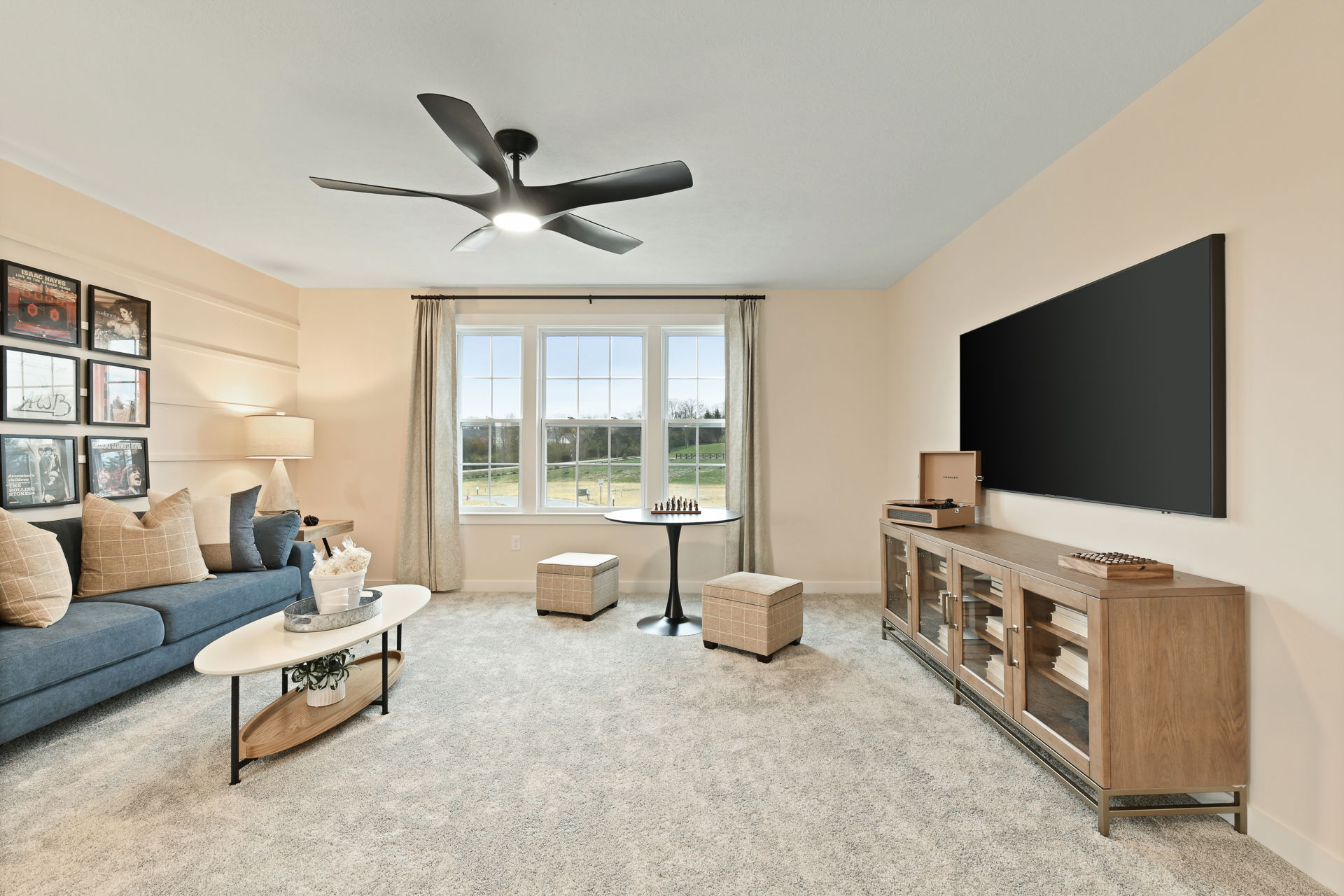 Modern living room with large ceiling fan, blue sofa, wall art, and a mounted flat-screen TV.