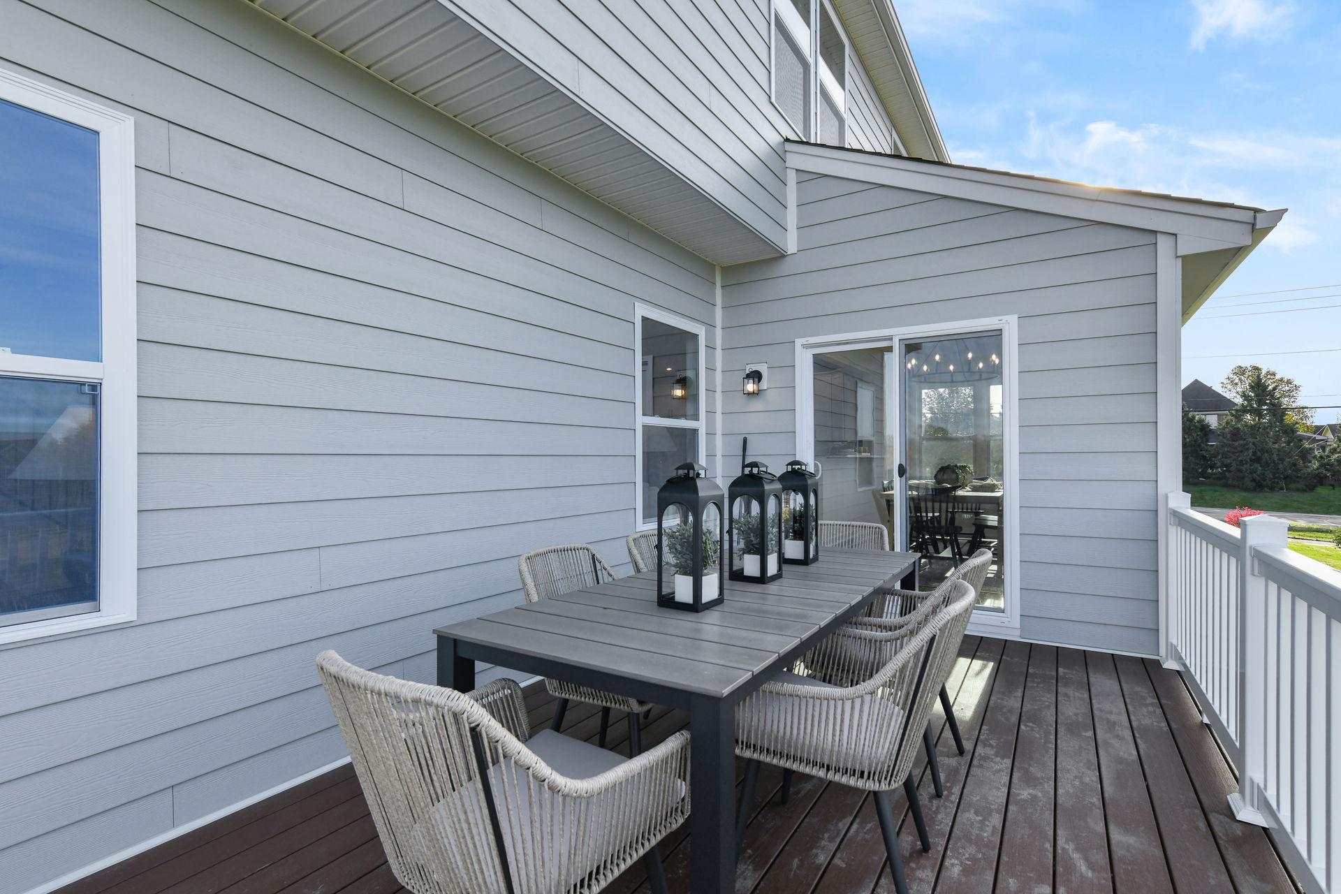 Outdoor patio with wicker chairs and a wooden dining table on a composite deck against a modern gray siding house.