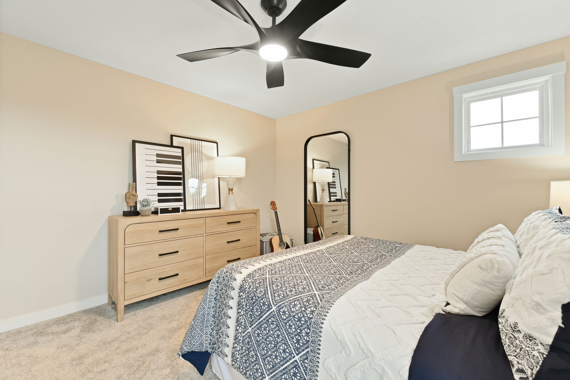 Modern bedroom interior with a stylish ceiling fan, wooden dresser, decorative artwork, and a cozy bed with patterned bedding.