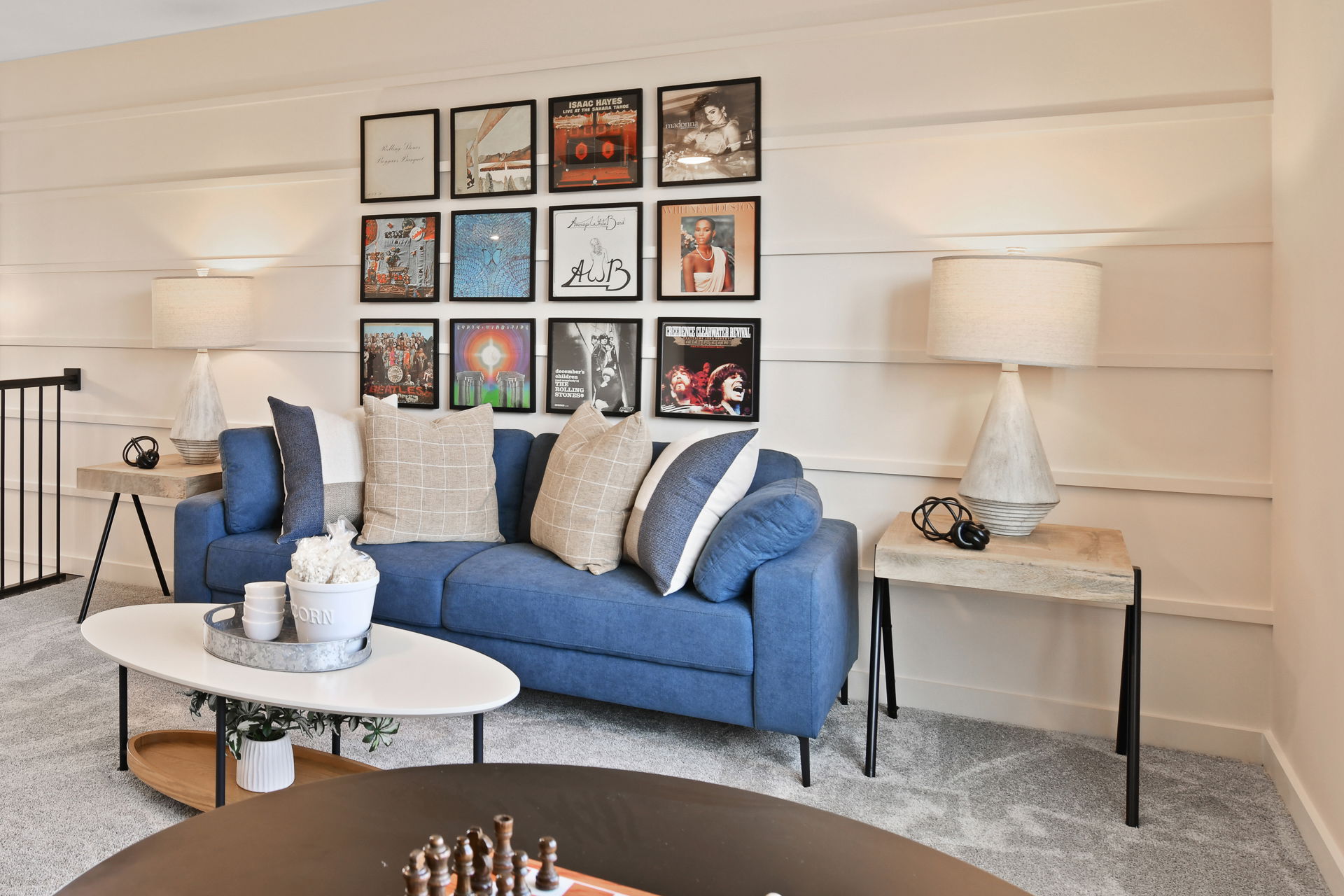Stylish living room featuring a blue couch, checkered pillows, wall-mounted record covers, and modern decor with ambient lighting.