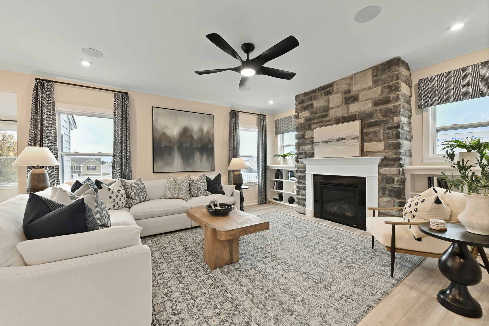 Stylish modern living room with a large sectional sofa, stone fireplace, wooden coffee table, and elegant decor.