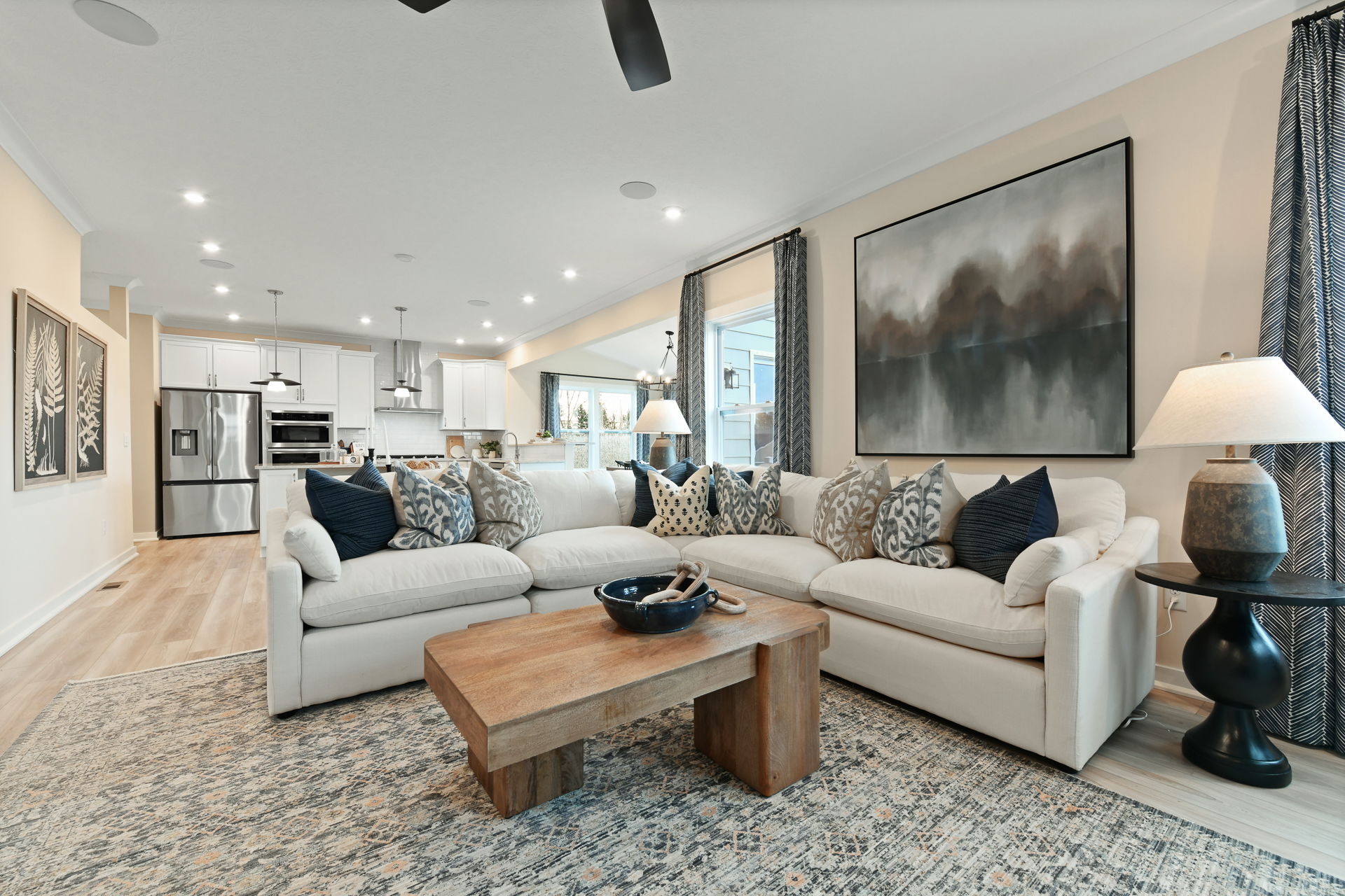 Stylish, modern open-concept living room with elegant decor, featuring a plush sectional sofa, wooden coffee table, and contemporary artwork.