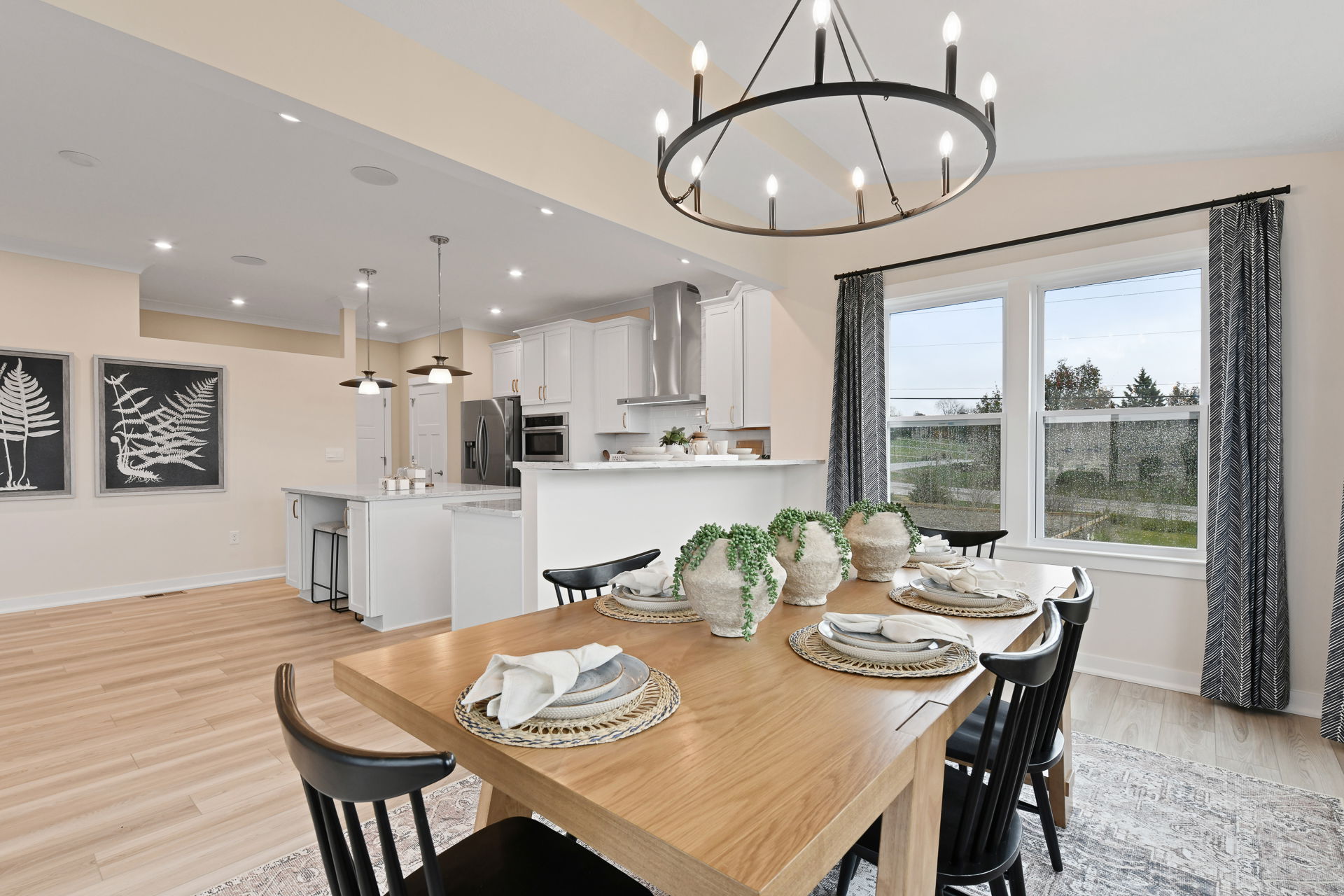 Modern open-concept kitchen and dining room with elegant wooden table, decorative plants, and contemporary lighting fixtures.
