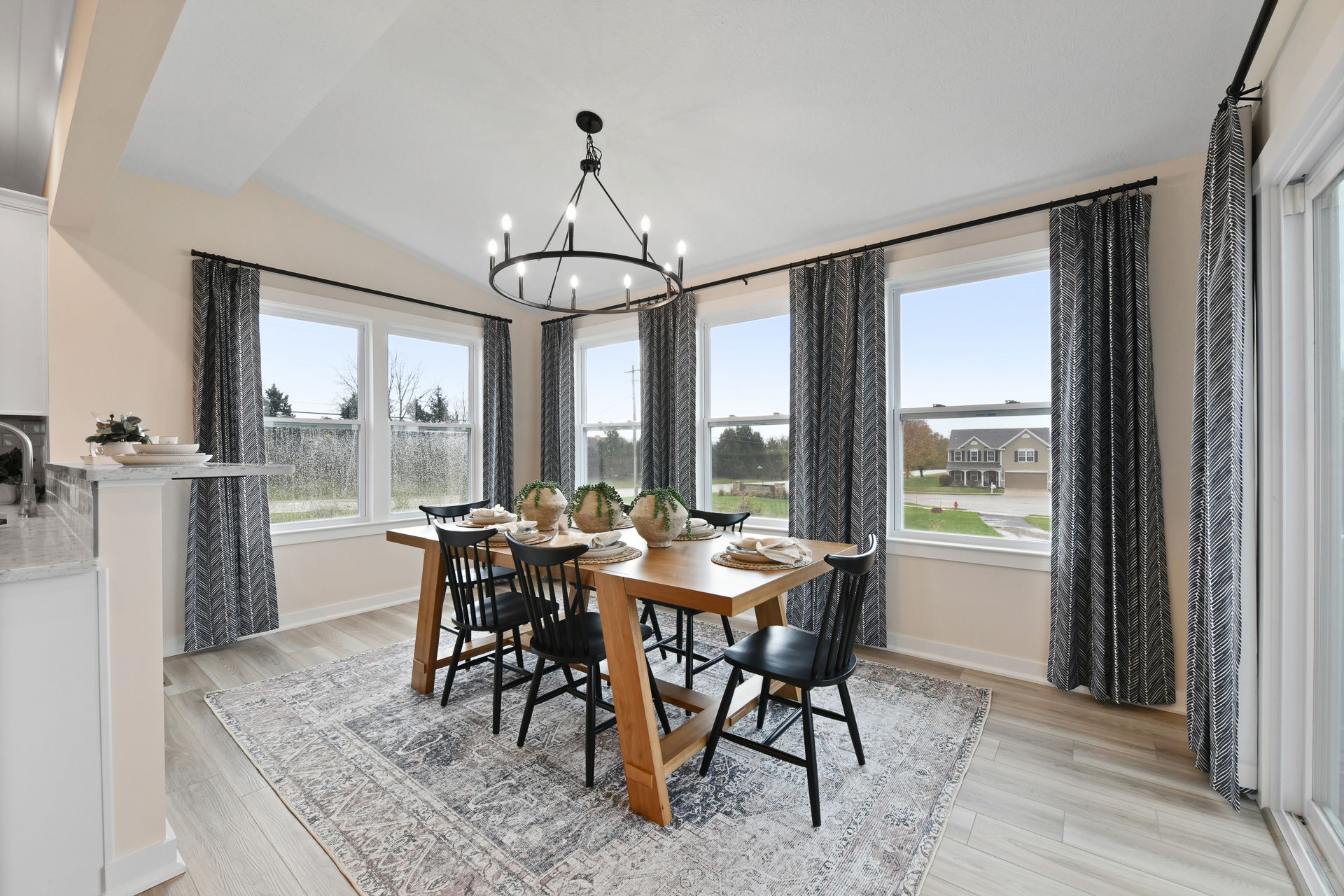 Bright, modern dining room with a wooden table, black chairs, and large windows featuring a view of the outside.