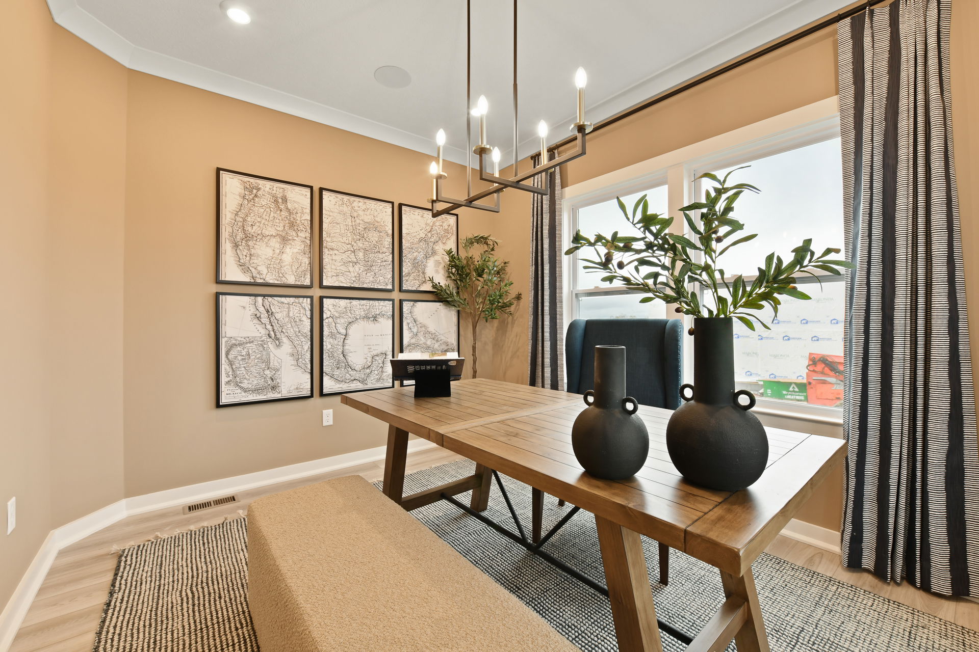 Contemporary dining room with a wooden table, black vases, map wall art, and large window with patterned curtains.