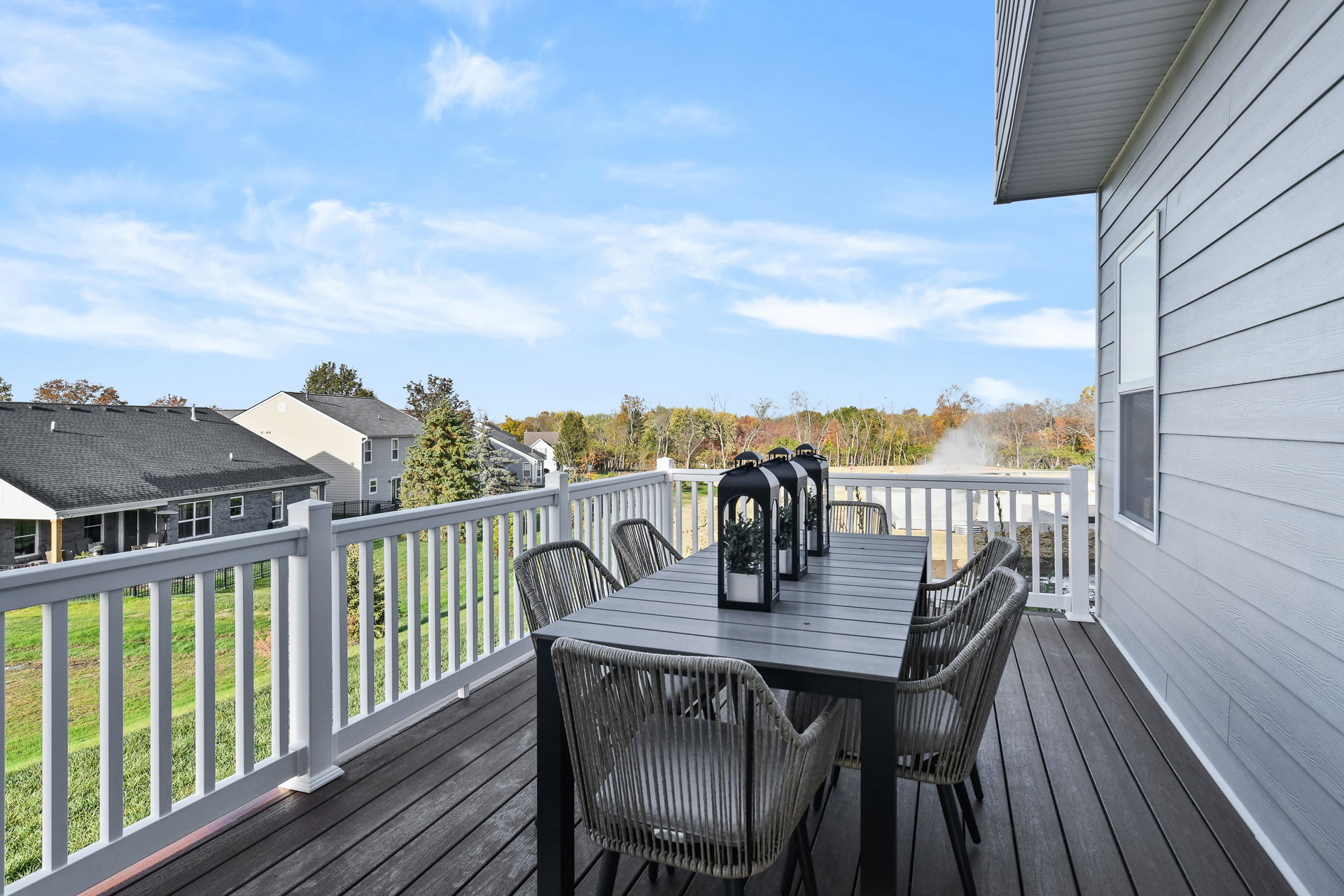 Spacious outdoor deck with a modern dining table set overlooking a suburban neighborhood and scenic landscape.