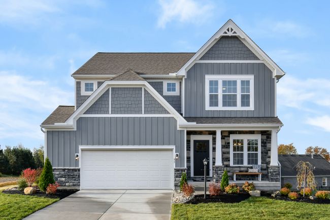 Two-story gray suburban house with white trim, a manicured lawn, and a spacious driveway under a clear blue sky.