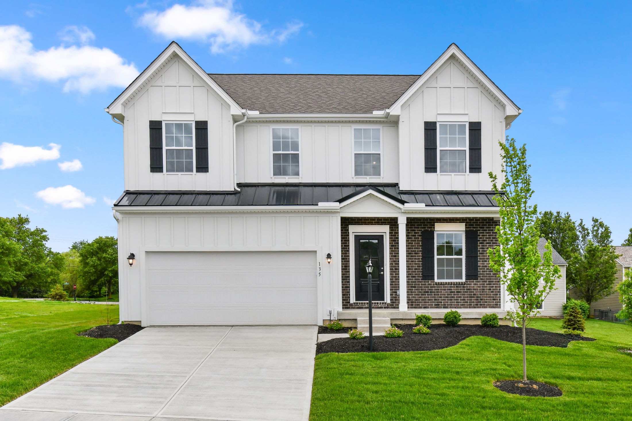Modern two-story suburban home with a black and white exterior, attached garage, and manicured lawn under a clear blue sky.