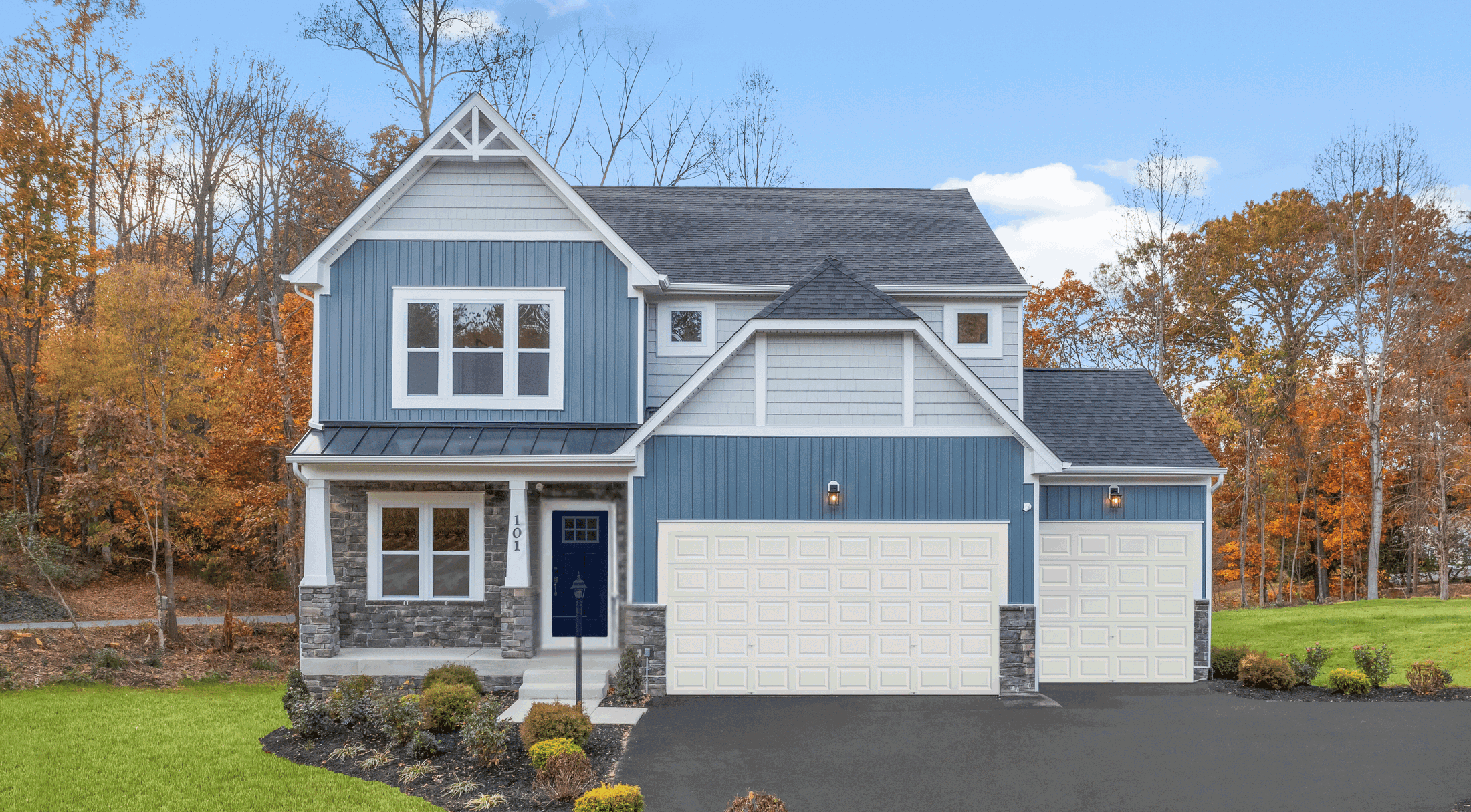 Modern blue house with stone accents and a two-car garage, surrounded by autumn foliage.