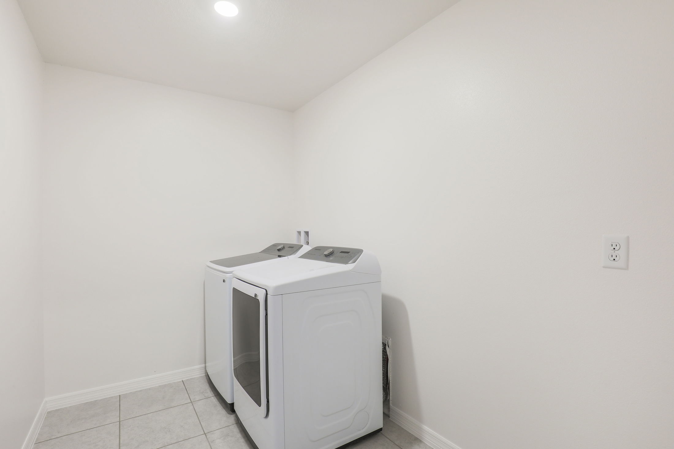 Minimalist laundry room with a modern white washer and dryer set against a light-colored wall and tiled flooring.
