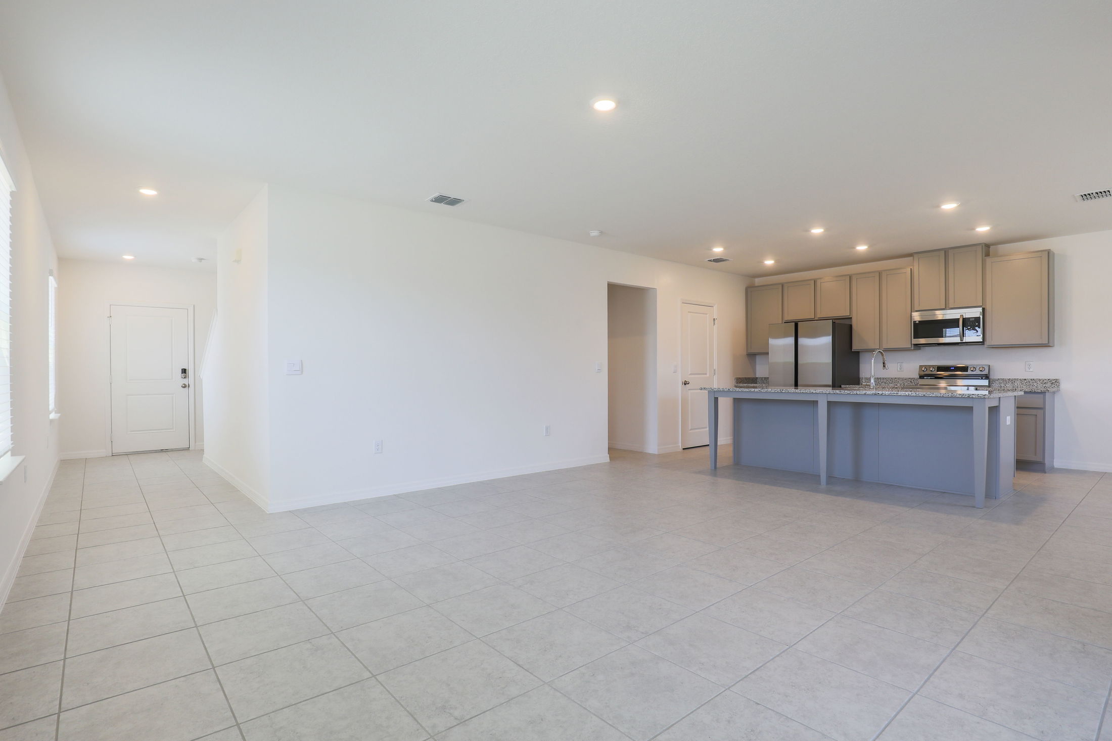 Modern open-concept kitchen and living area with gray cabinetry, granite countertops, and tiled flooring in a bright, spacious home interior.