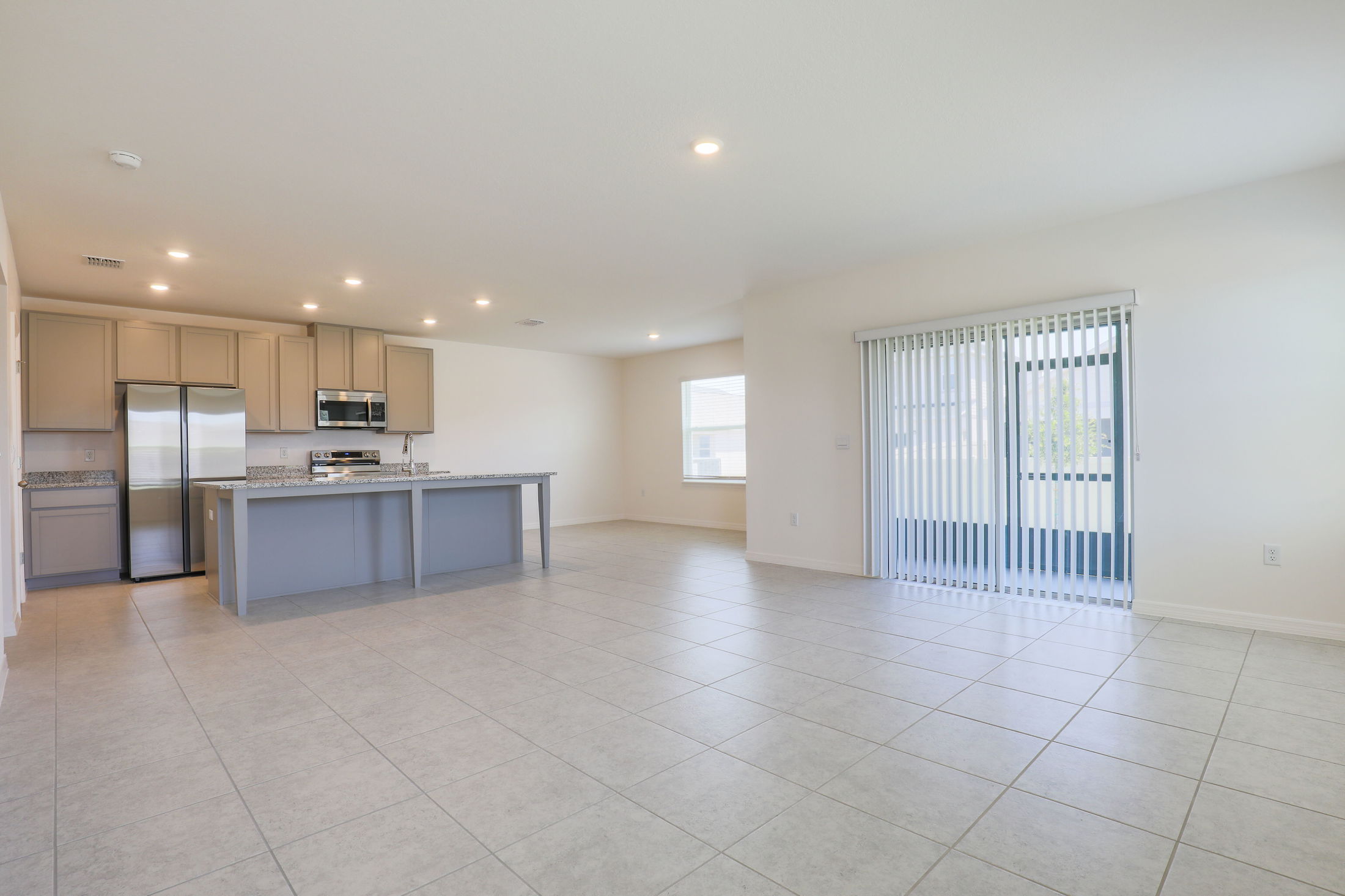 Spacious modern kitchen with granite countertops, stainless steel appliances, and an open-plan design in a bright, empty home interior.