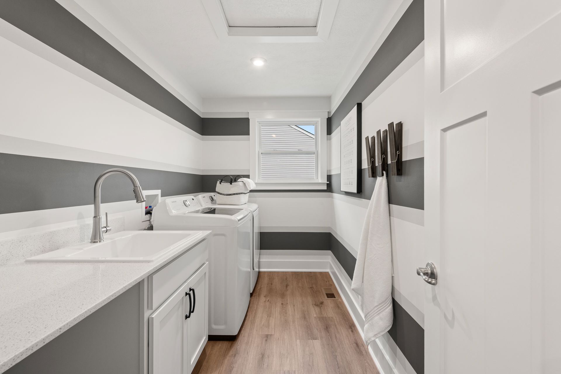 Modern laundry room with striped walls, featuring a washing machine, dryer, sink, and wood flooring.