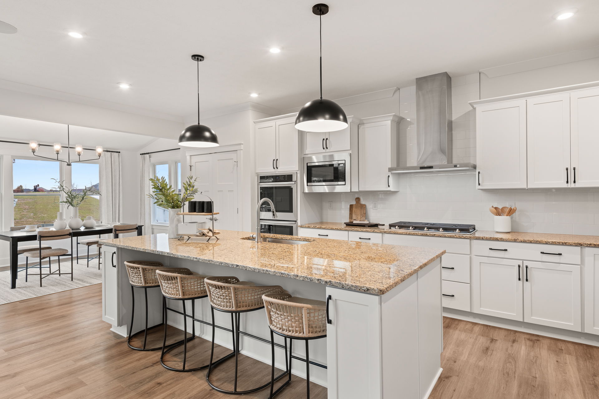 Modern kitchen with white cabinets, granite countertops, and black pendant lighting above a spacious island with bar stools.