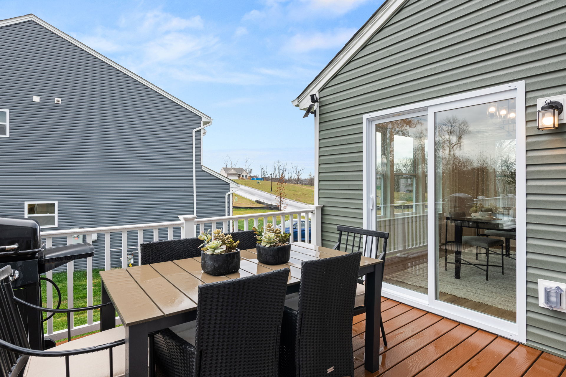 Modern backyard deck with outdoor dining set and potted plants, adjacent to a sliding glass door.