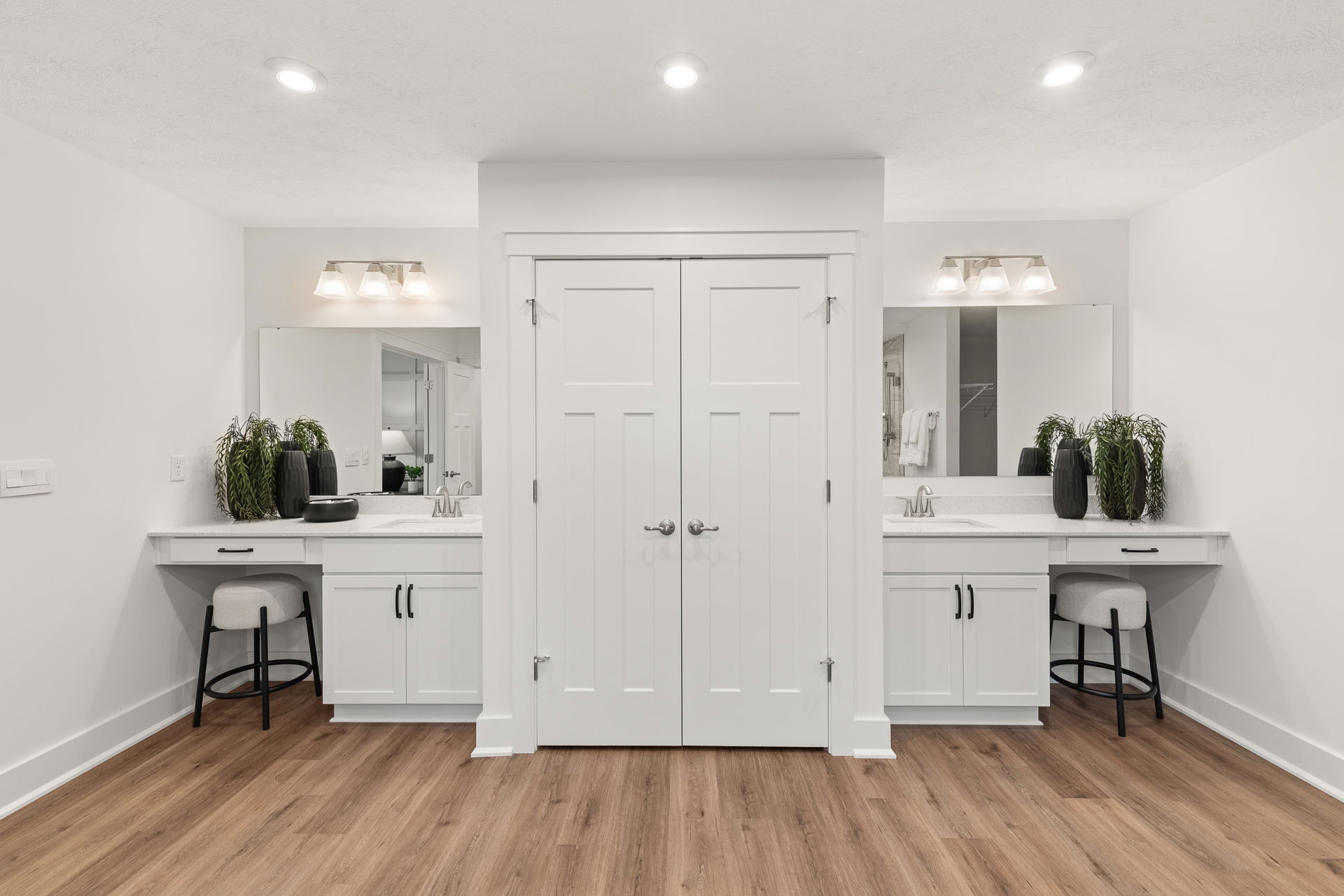 Modern bathroom with dual vanities, white cabinets, large mirrors, and wooden flooring.