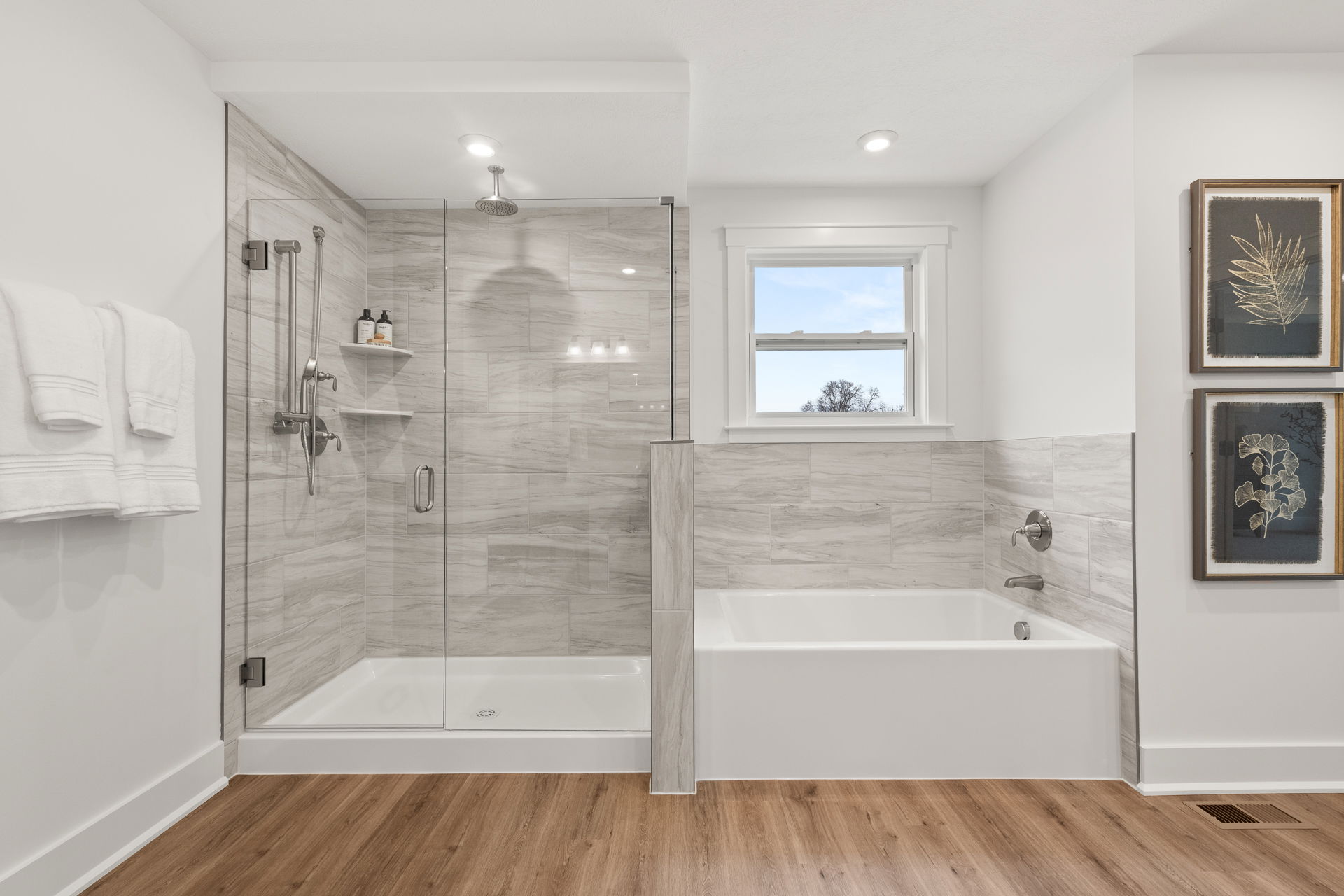 Modern bathroom featuring a glass-enclosed shower, bathtub, and wood-style flooring with contemporary wall decor.