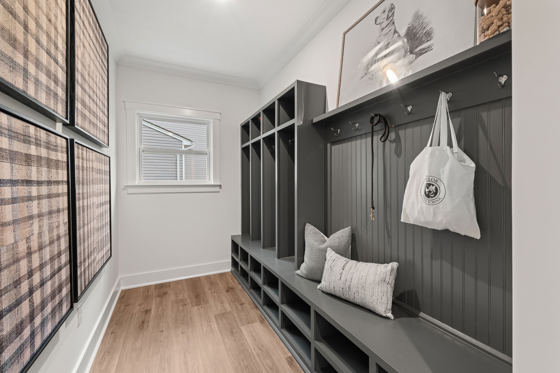 Modern mudroom with dark gray storage cubbies, hooks, and cozy seating, accented with decorative art and a window providing natural light.