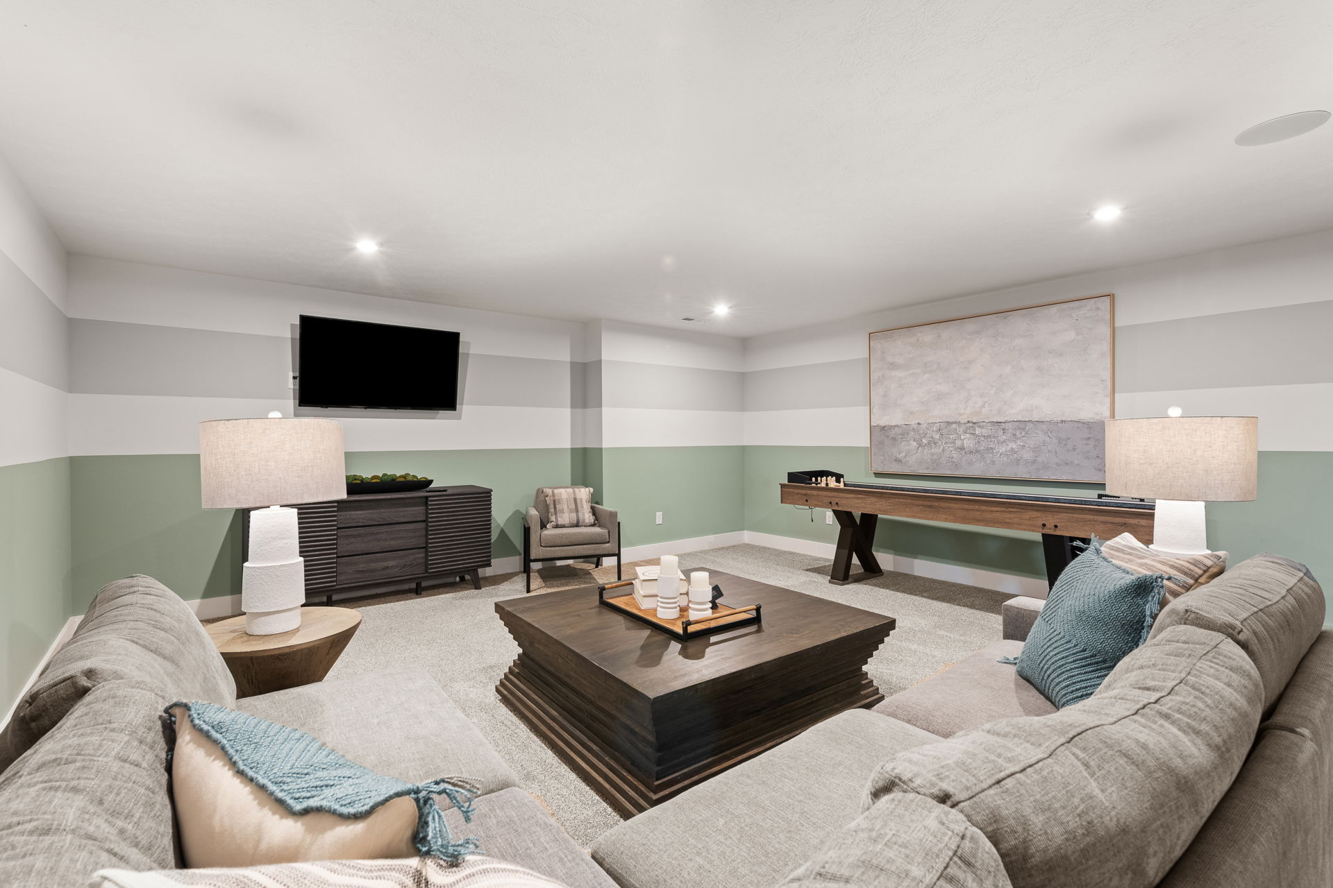 Spacious basement entertainment room with a sectional sofa, striped wall design, TV, and shuffleboard table.