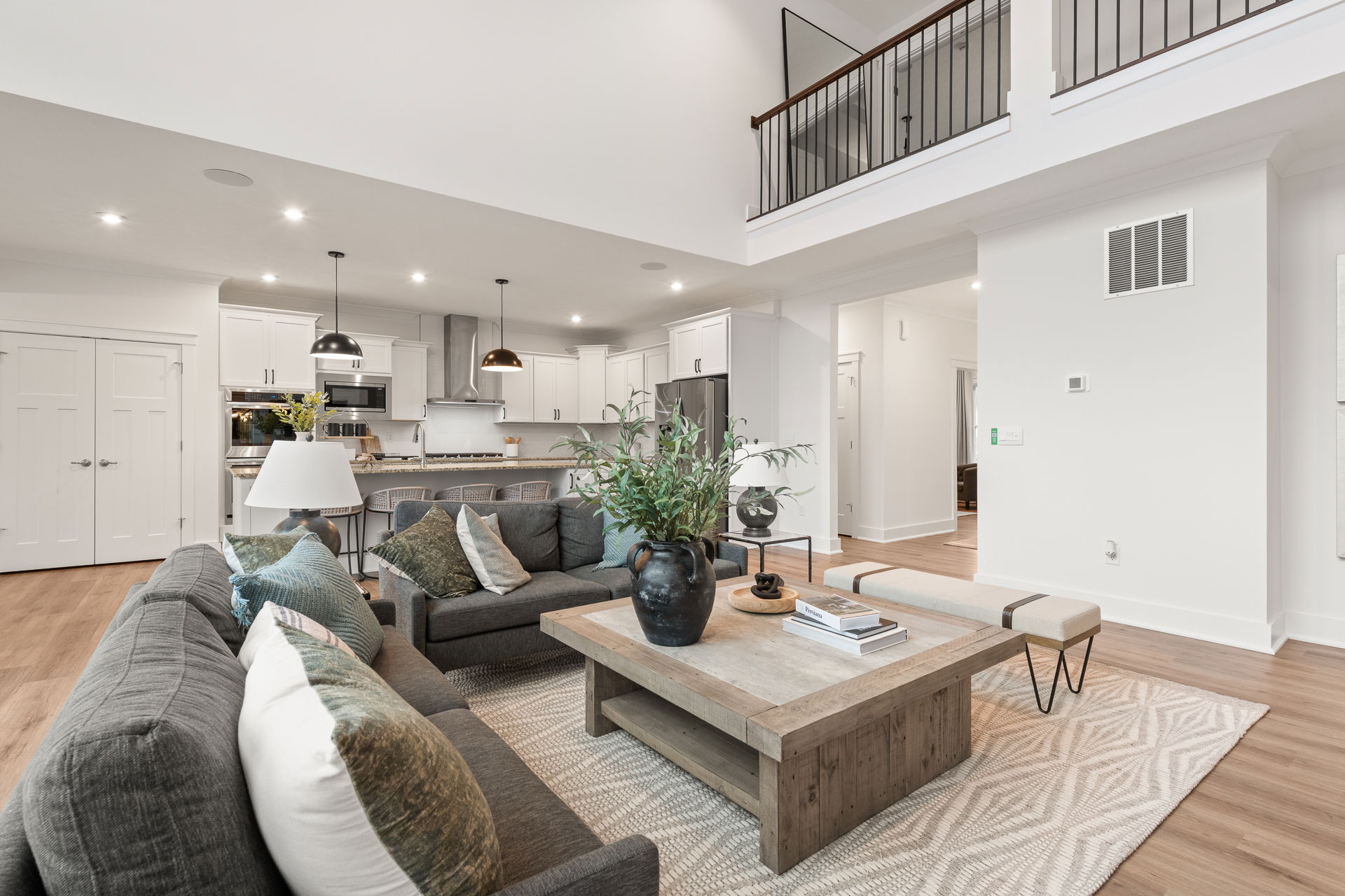 Modern open-concept living room with stylish decor, featuring a cozy grey sofa, large wooden coffee table, and sleek kitchen in the background.
