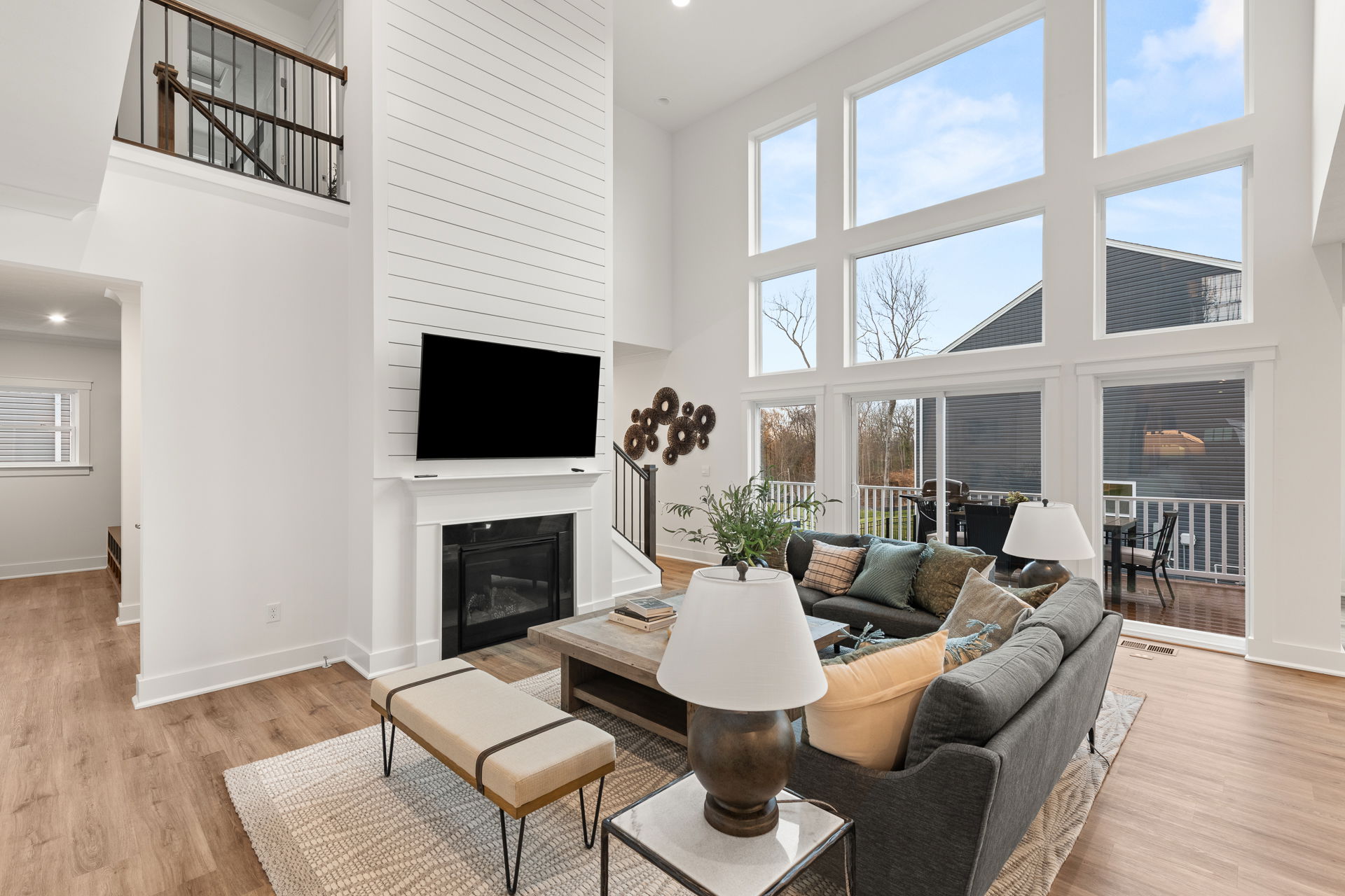 Modern living room with large windows, cozy seating area, fireplace, and a wall-mounted TV in a bright, open-concept design.