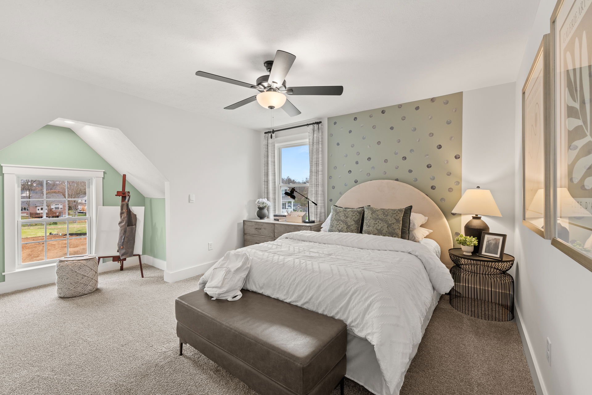 Cozy modern bedroom with neutral decor, featuring an elegant bed, two bedside tables with lamps, wall art, and a large window overlooking a suburban neighborhood.