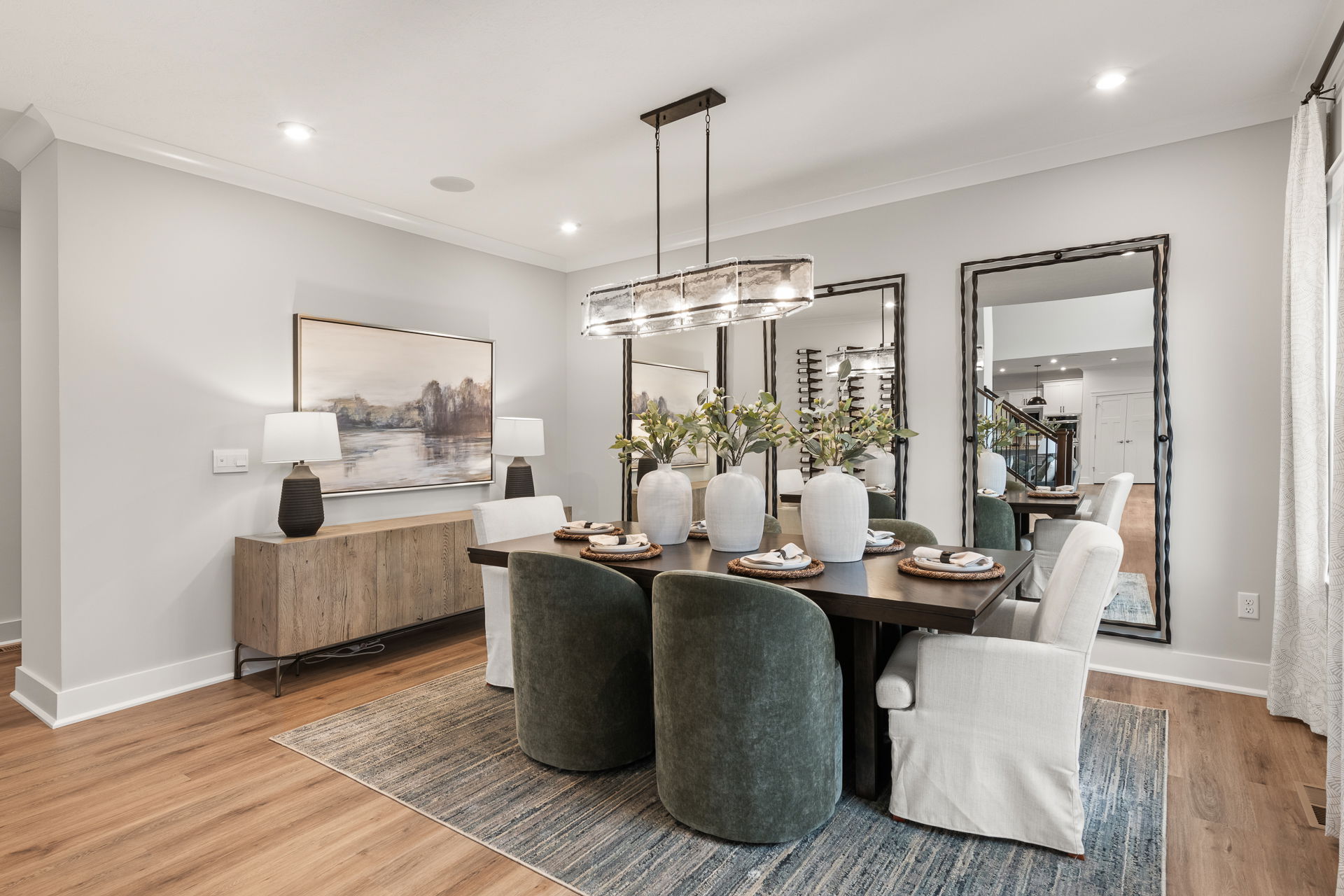 Elegant modern dining room with a dark wooden table, green and white upholstered chairs, decorative vases, and stylish lighting fixtures.