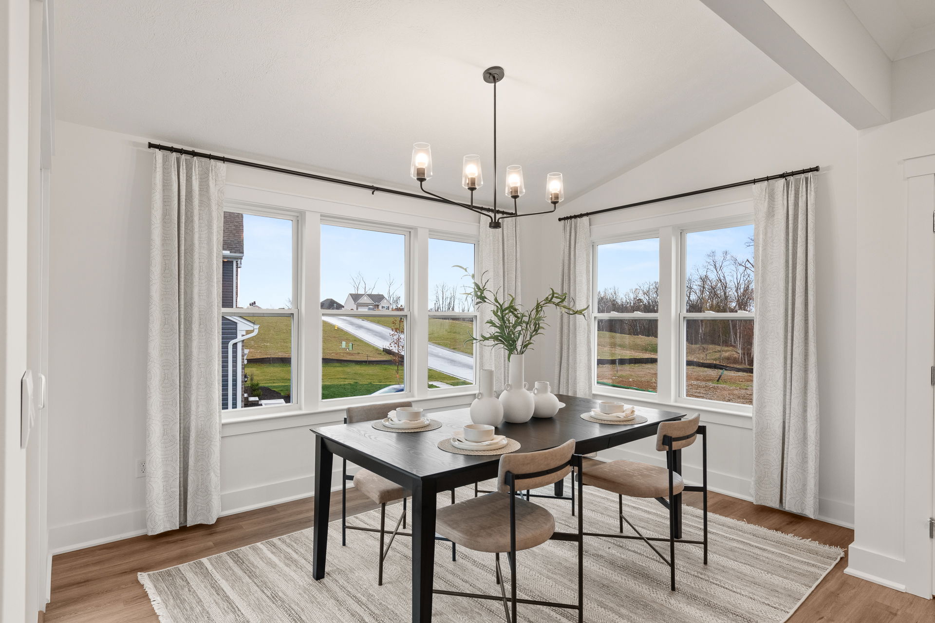 Modern dining room with a black table, four chairs, decorative vases, and large windows showcasing a scenic outdoor view.