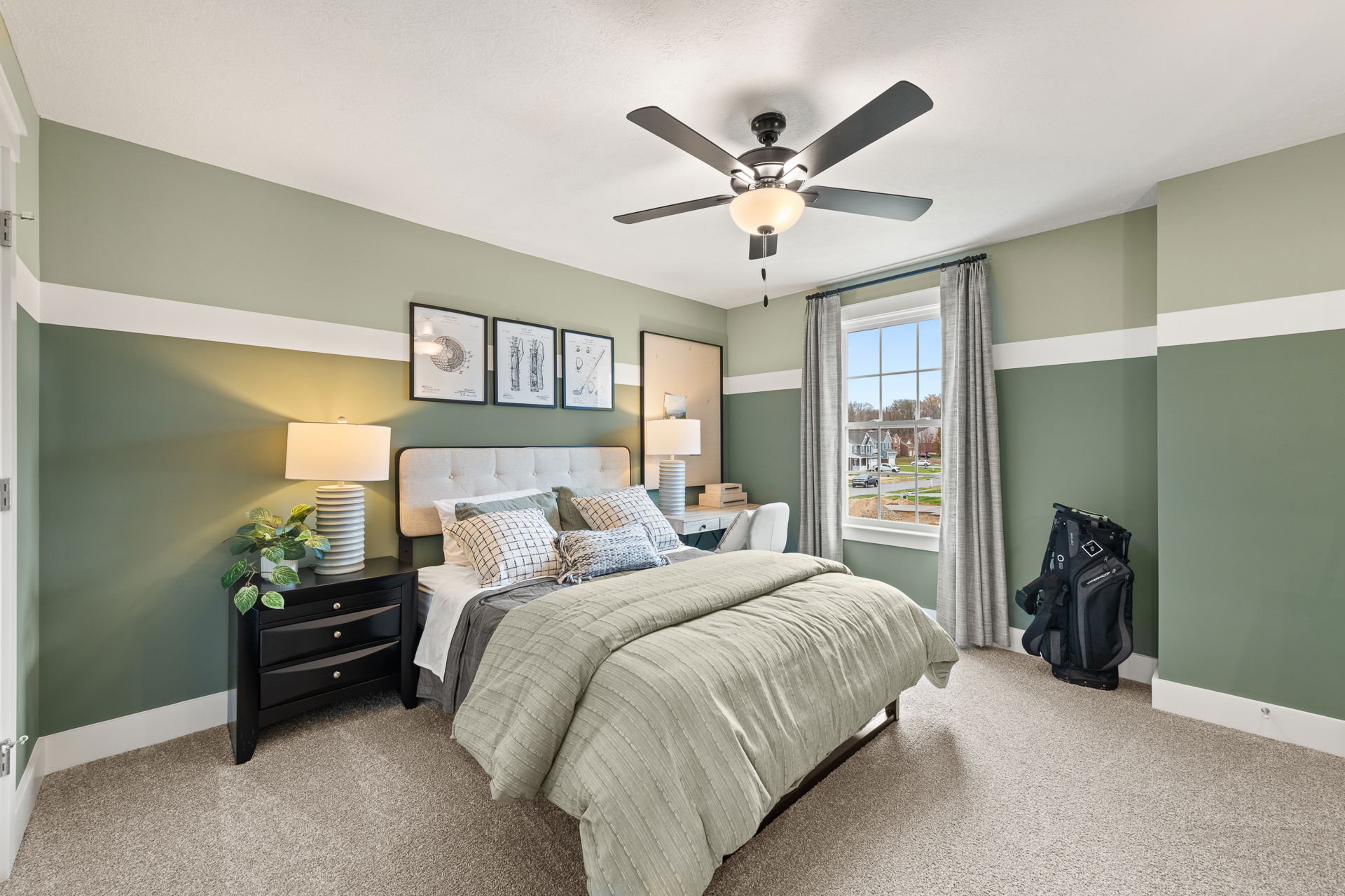 Modern bedroom with green and white walls, featuring a cozy bed, wall art, ceiling fan, large window, and bedside tables with lamps.