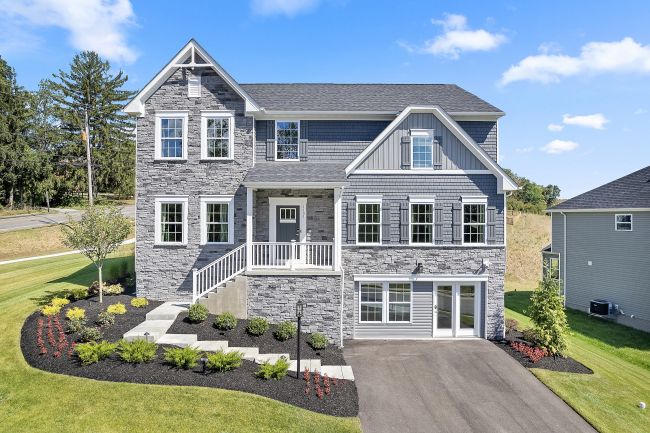Modern two-story stone house with landscaped front yard and driveway on a sunny day.