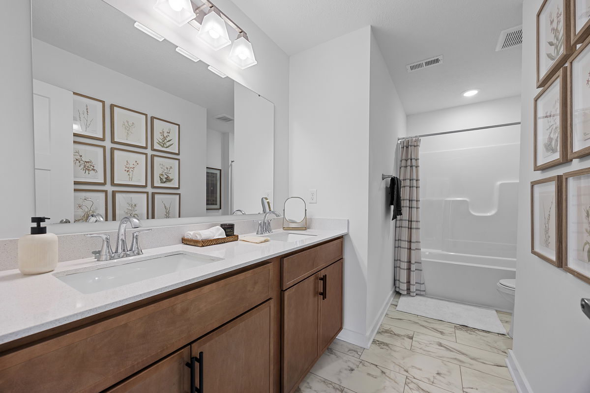Modern bathroom with dual sink vanity, framed botanical wall art, and a sleek shower area.