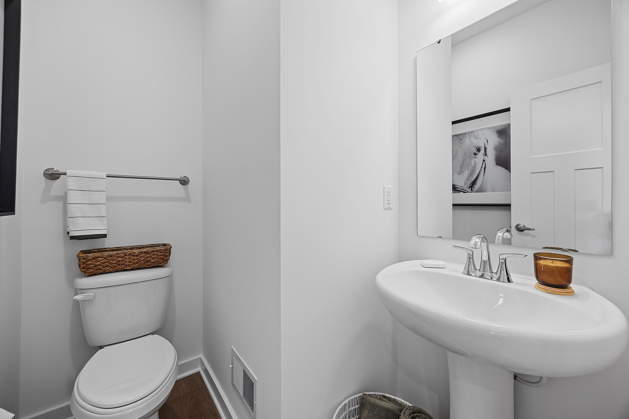 Modern minimalist bathroom with a white pedestal sink, toilet, and a towel rack featuring a wicker basket and decor.