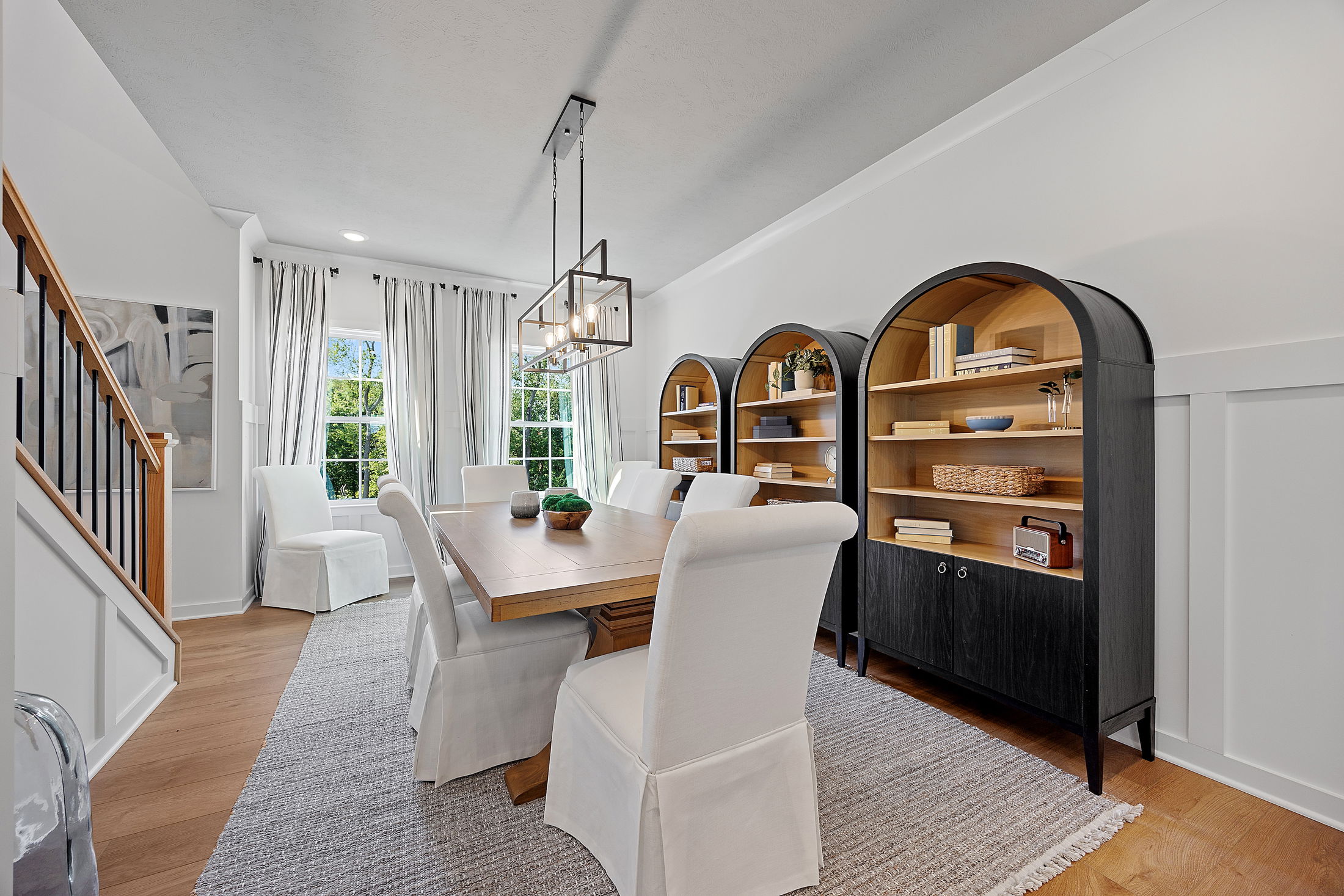 Elegant dining room with a wooden table, white upholstered chairs, modern light fixture, and built-in bookshelves.