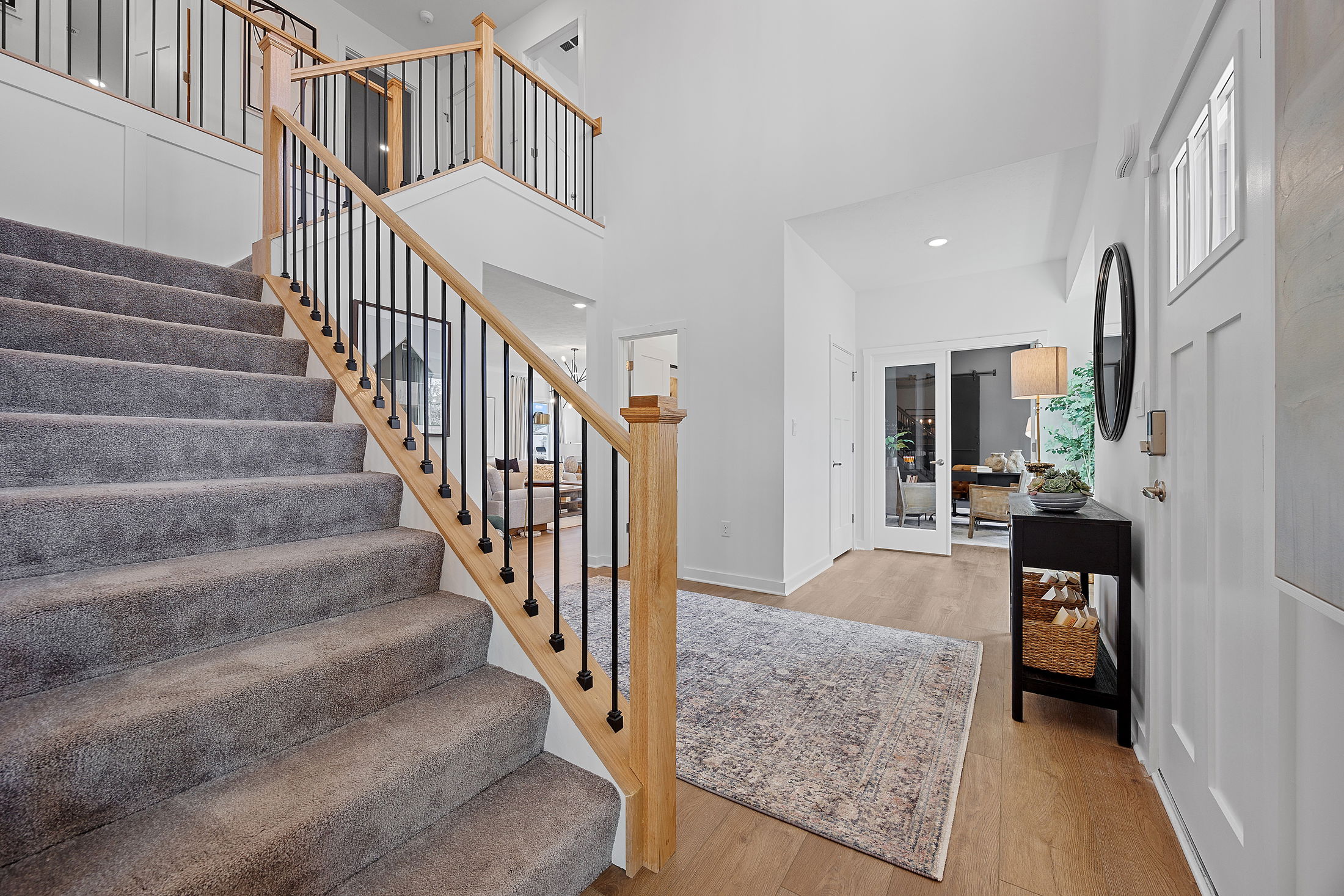 Modern home foyer with carpeted staircase, wooden railings, and a stylish entryway leading to a living room.