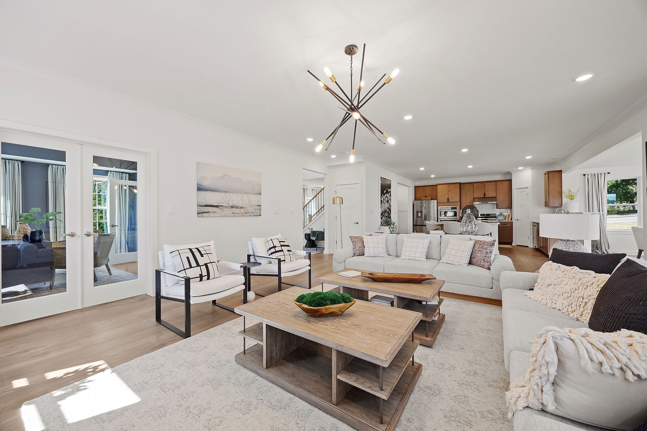 Modern open-concept living room with stylish lighting, a neutral color palette, and a view into the kitchen.