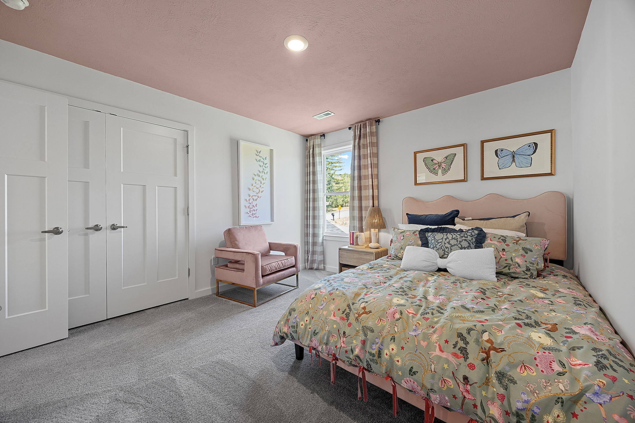 Colorful, cozy bedroom with a pink ceiling, butterfly artwork, and a floral-patterned bedspread.