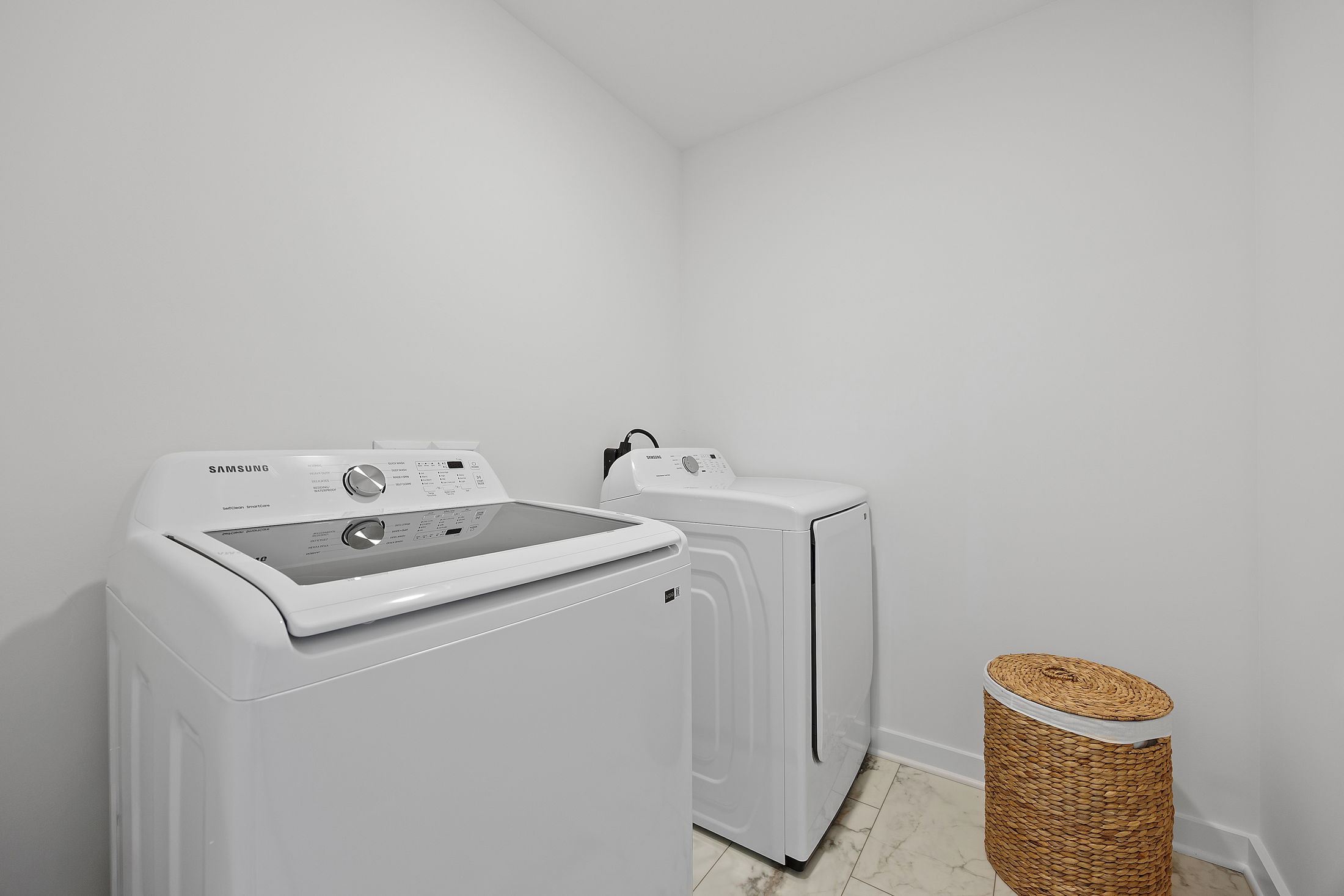 Modern laundry room with Samsung washer and dryer beside a wicker laundry basket.