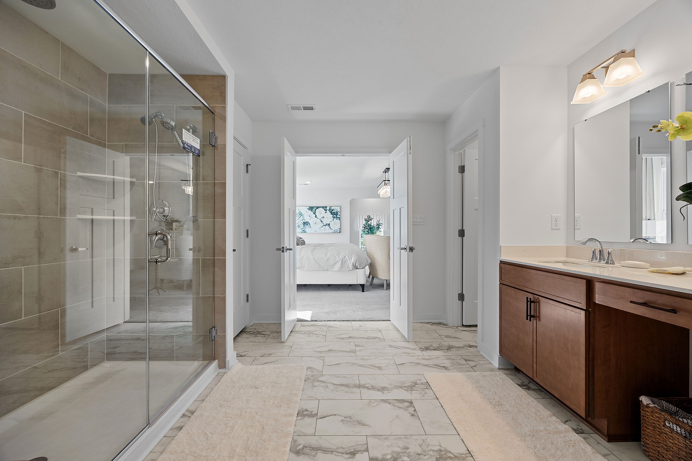 Modern bathroom interior with marble flooring, glass shower, and wooden vanity leading to a cozy bedroom.