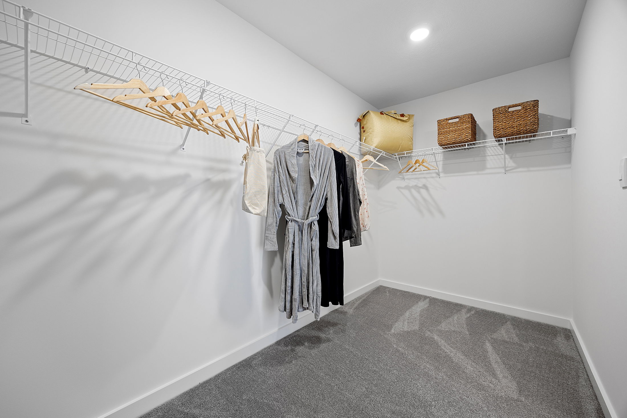 Spacious walk-in closet featuring organized shelving, wooden hangers, clothing items, and storage baskets under bright lighting.