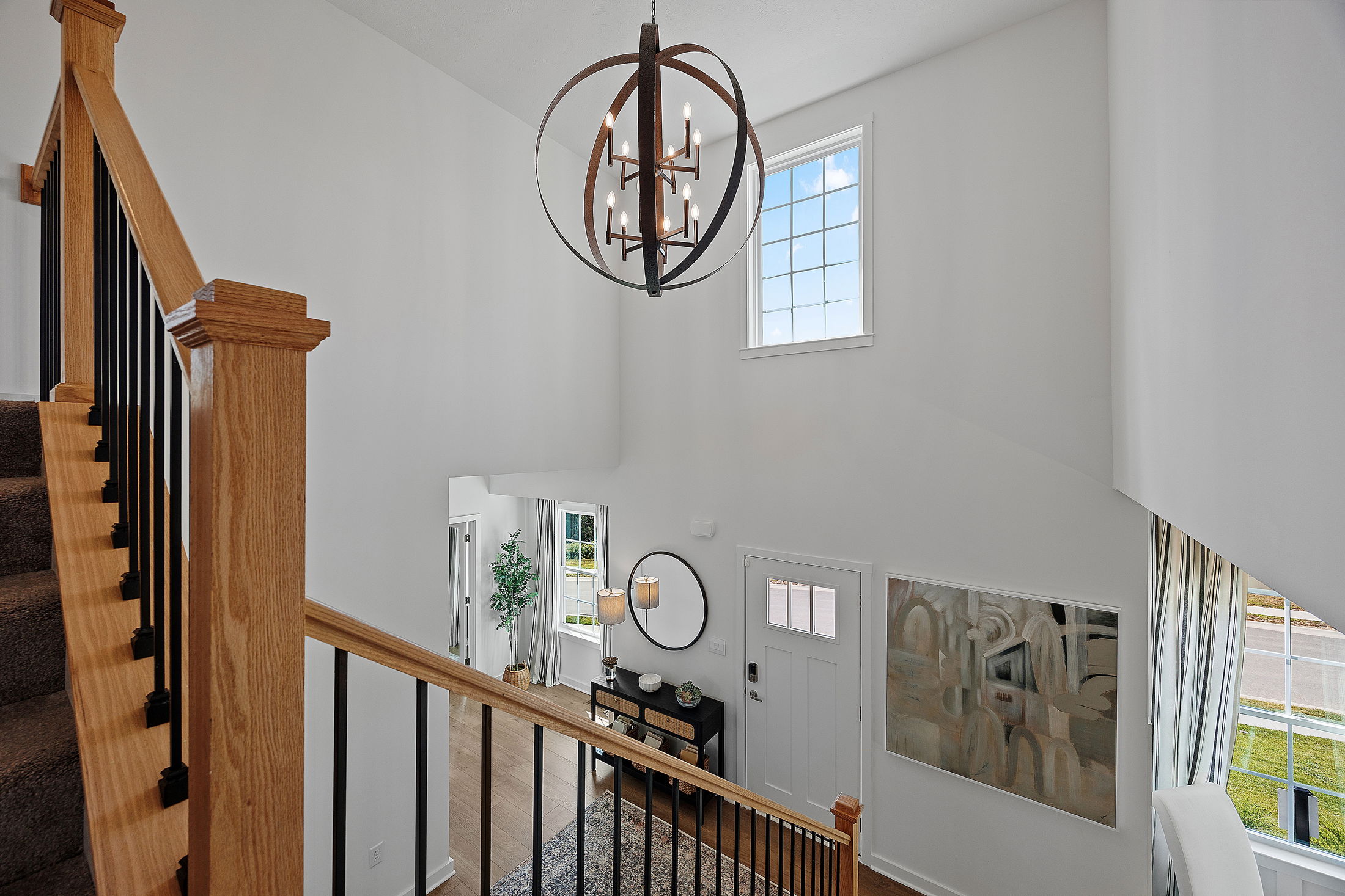 Modern home entryway with wooden staircase, large chandelier, and decorative console table in a bright, airy space.