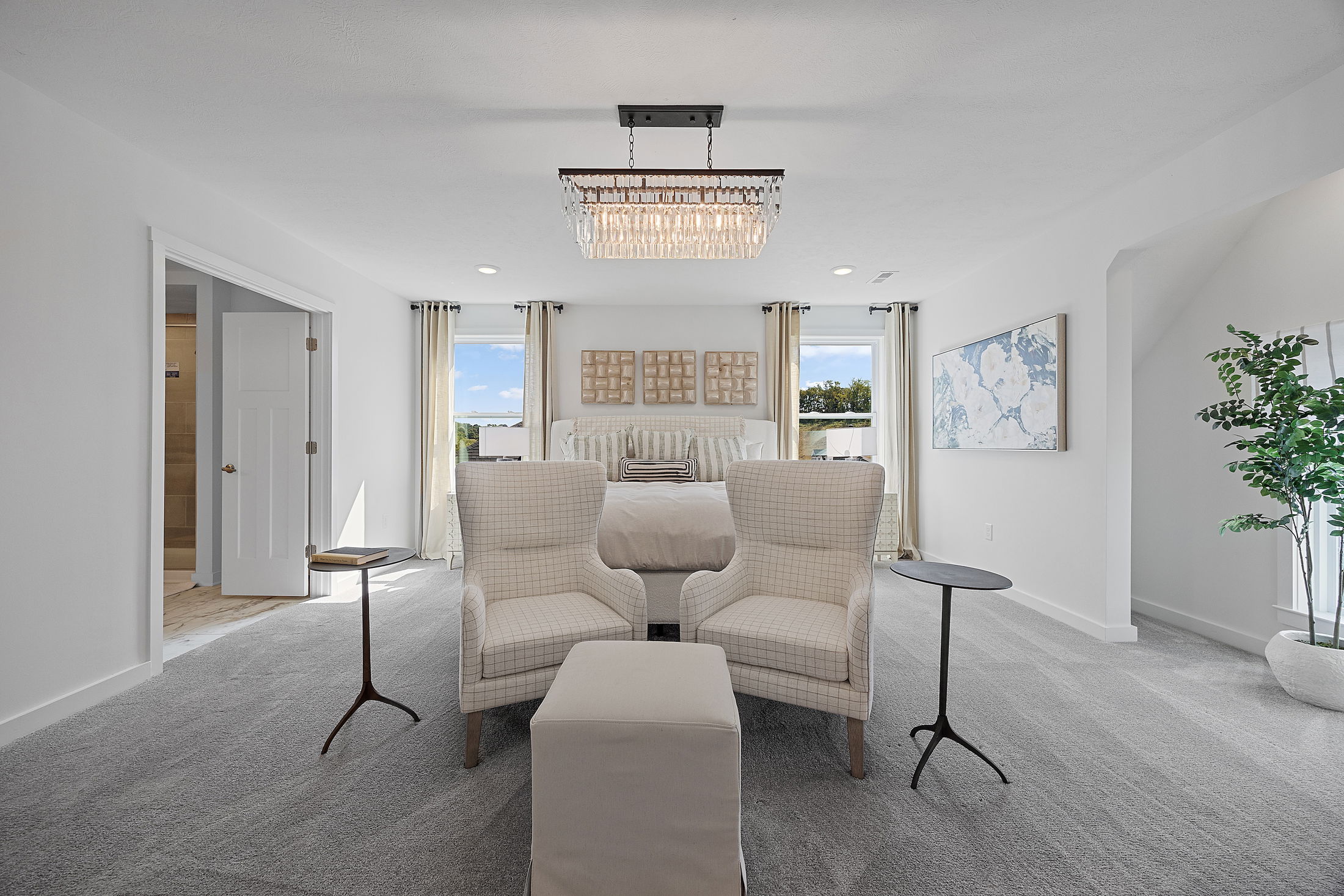 Spacious modern bedroom with elegant decor, featuring two armchairs, a plush bed, and a chic chandelier.
