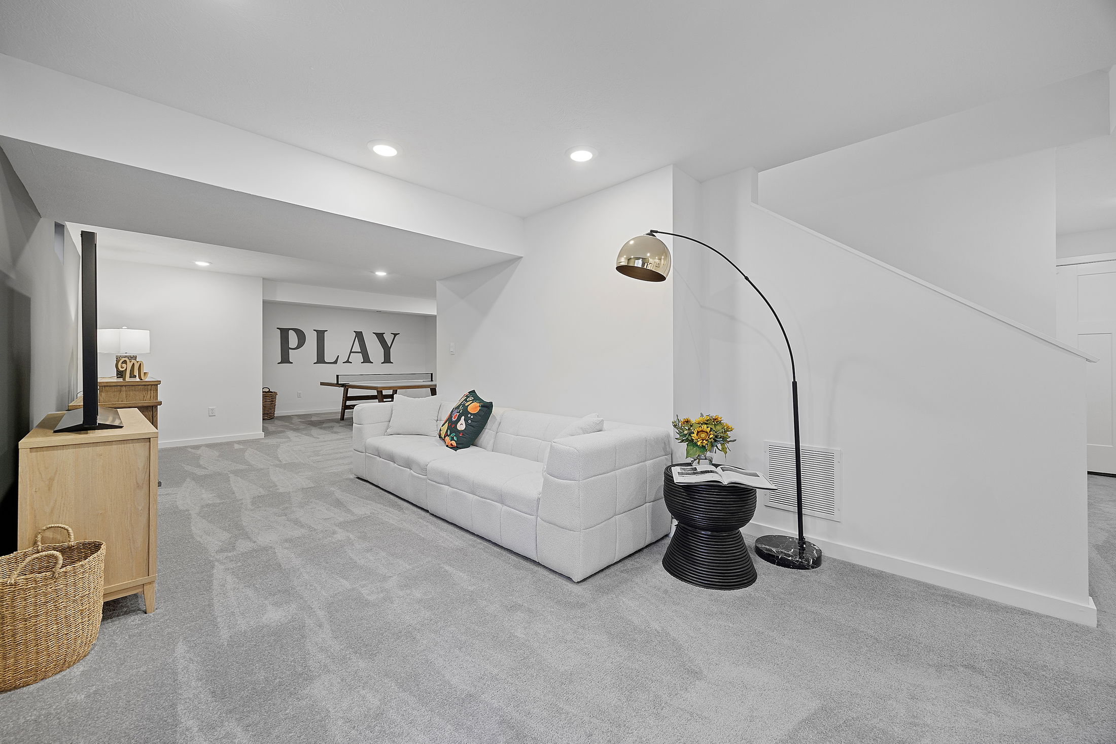 Modern basement entertainment room with a cozy white sofa, large TV, and a ping pong table.