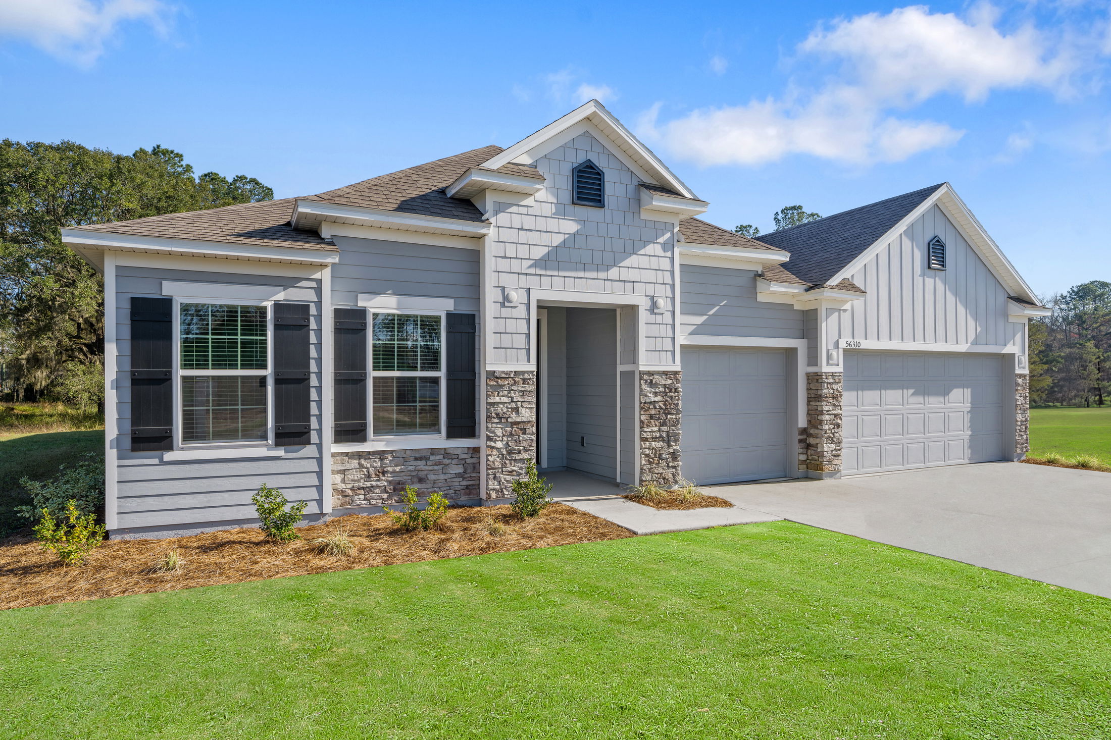 Modern gray suburban house with stone accents, large windows, and a three-car garage set against a clear blue sky.