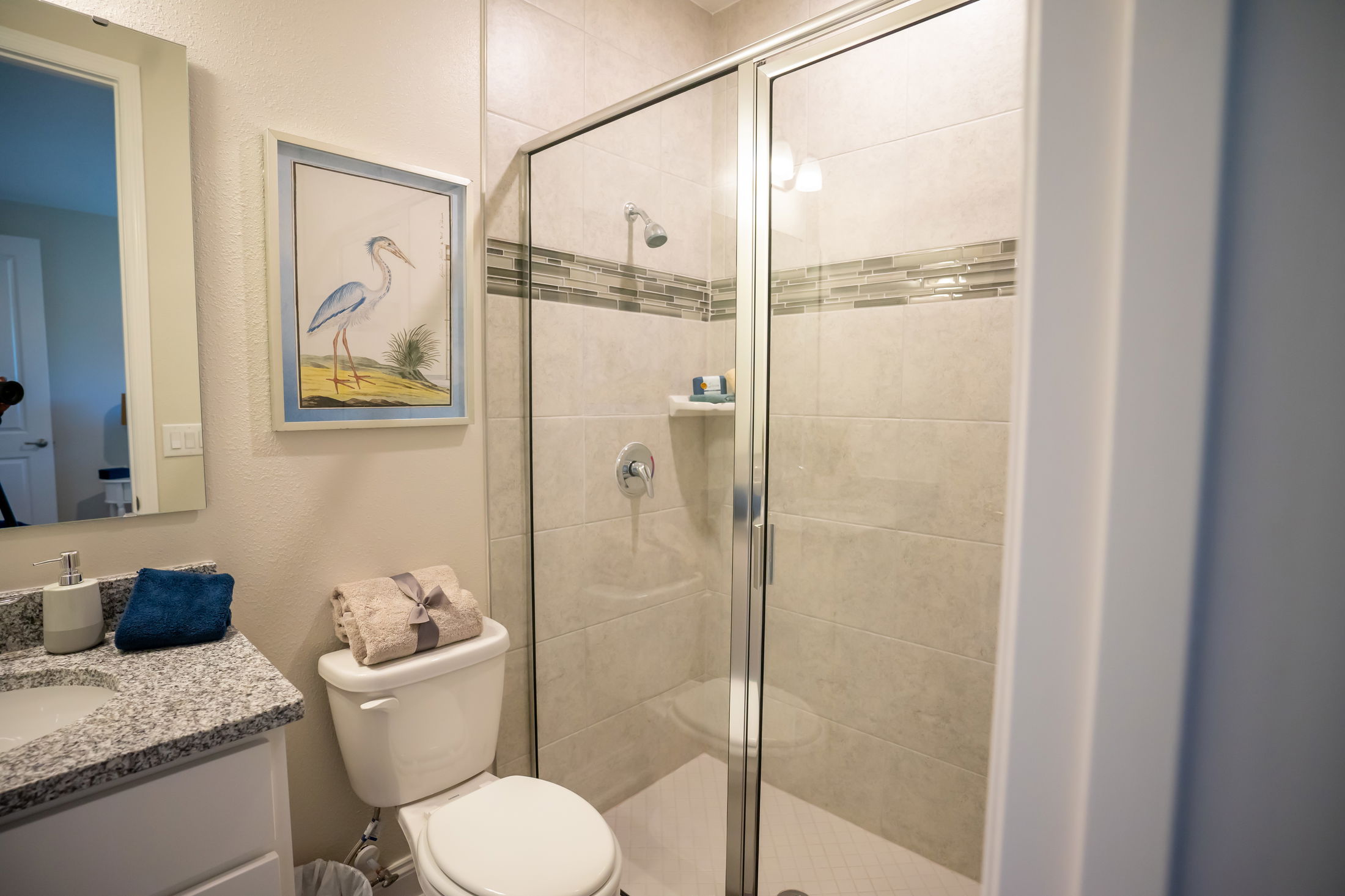 Modern bathroom with a glass-enclosed shower, granite countertop, and heron artwork on the wall.