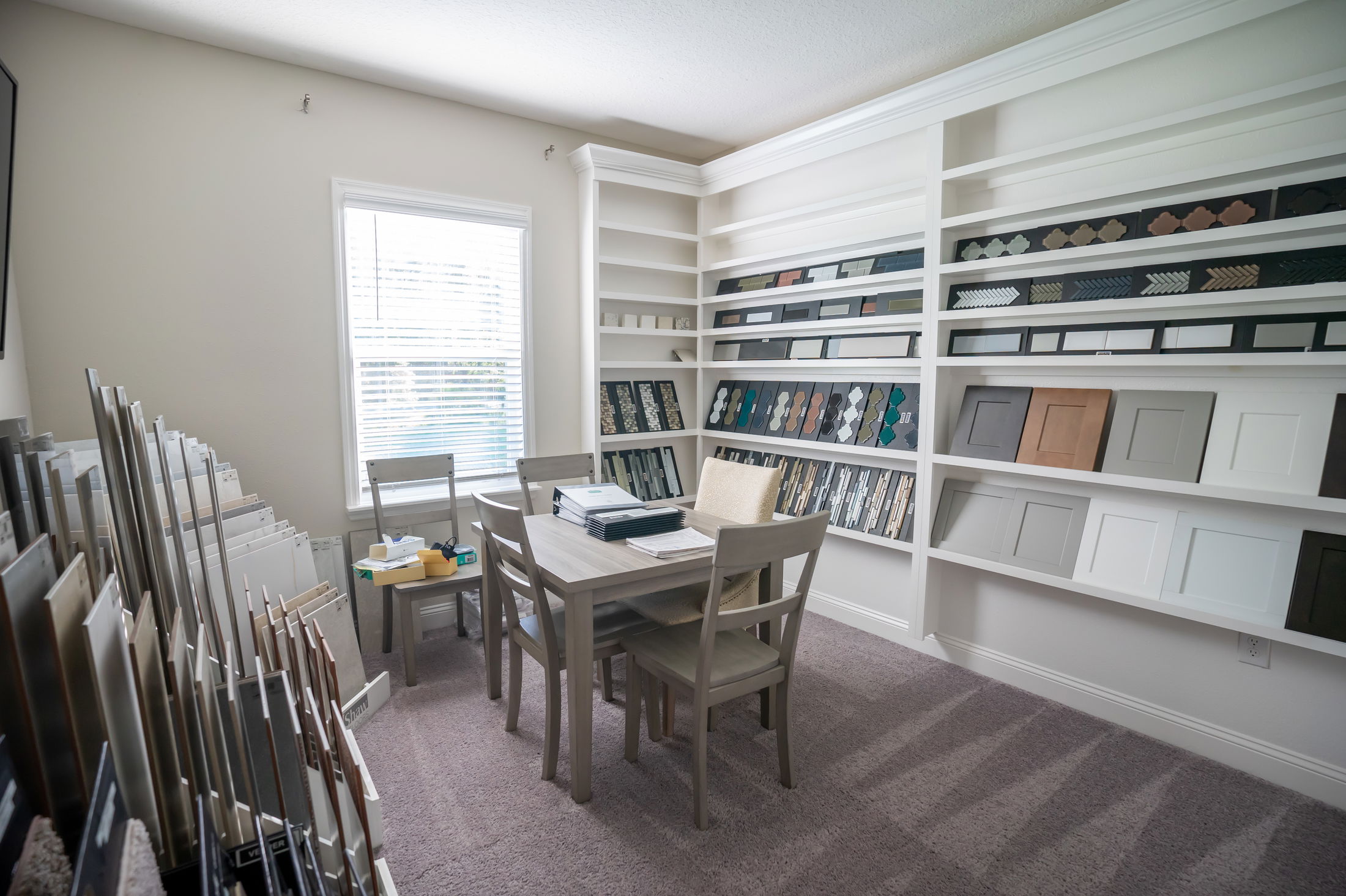 Small modern showroom featuring interior design samples, including cabinet doors and countertop materials, displayed on shelves around a consultation table.