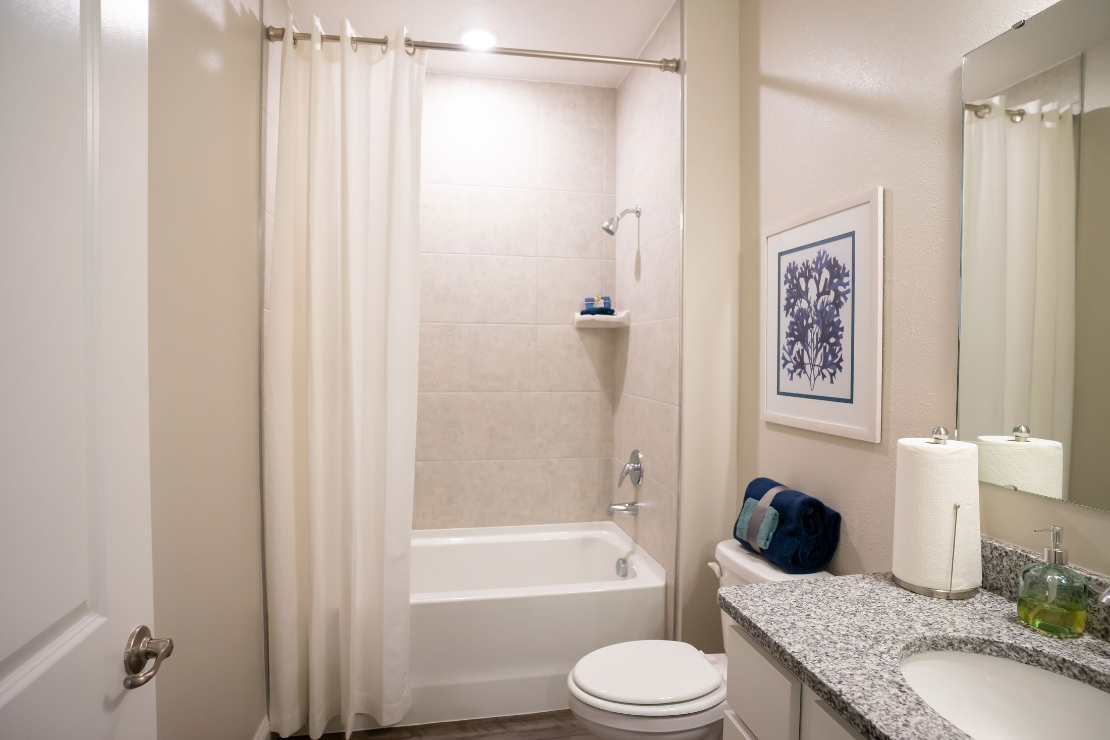 A modern bathroom with a granite countertop, white shower curtain, and neatly arranged towels.