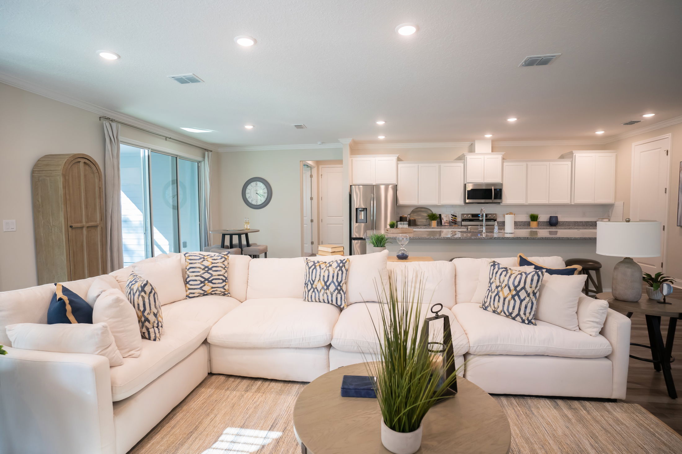 Modern open-concept living room with a large white sectional sofa, elegant throw pillows, and a view into a contemporary kitchen.