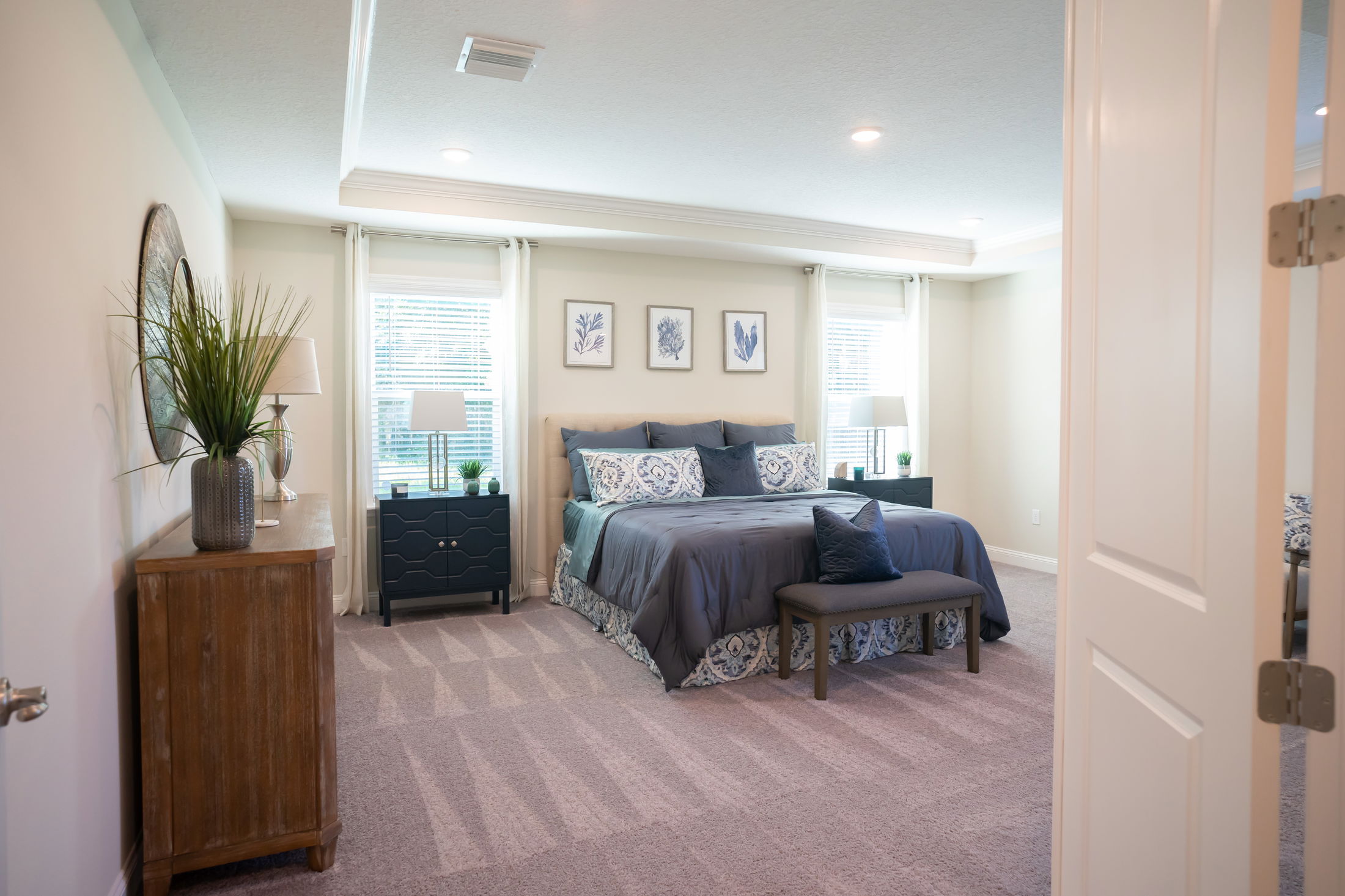 Modern bedroom interior with a neatly made bed, decorative pillows, wooden furniture, and framed art on the walls.