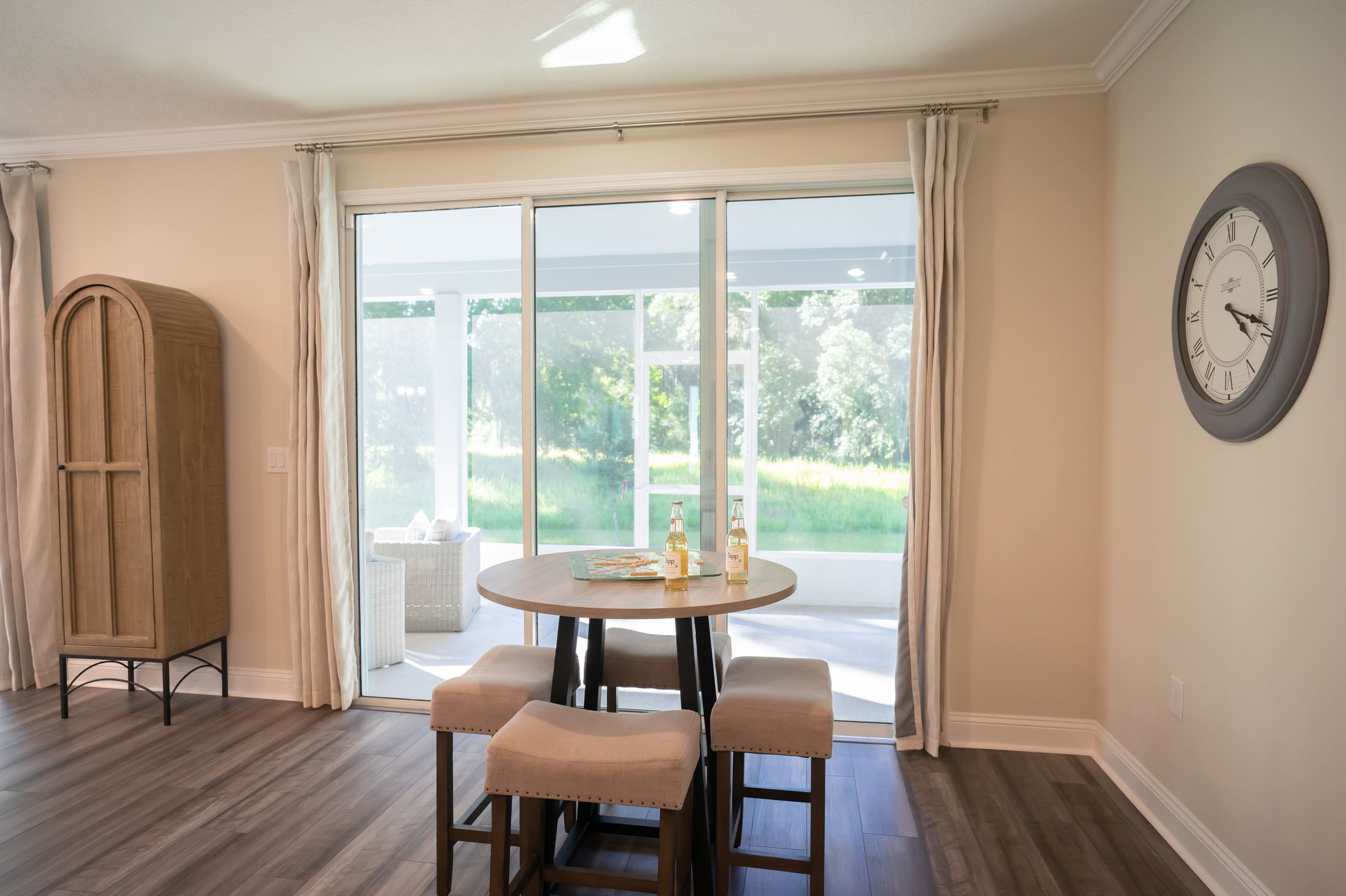 Bright dining area with round table, four stools, large sliding glass doors, and picturesque garden view.